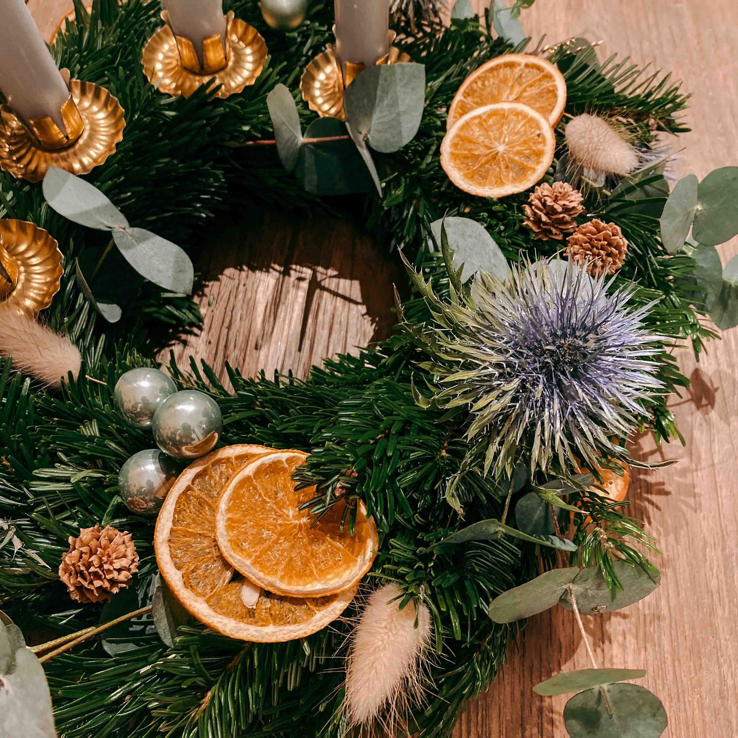 Getrocknete Orangenscheiben, blaue Blumen und grüne Kugeln auf Adventskranz Sterntaler.