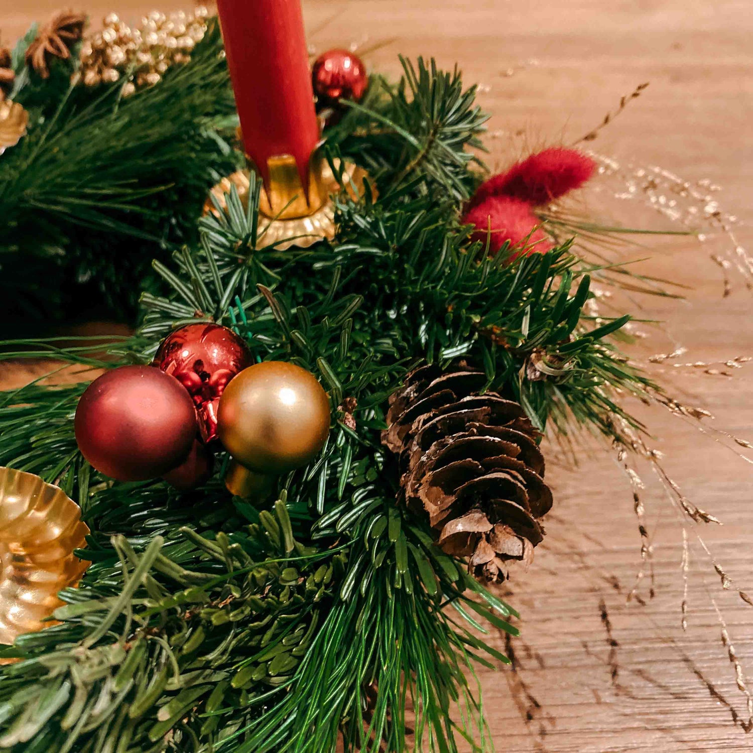 Nahaufnahme roter und goldener Kugeln auf Tannengrün – Adventskranz Rotkäppchen in Naturtönen.