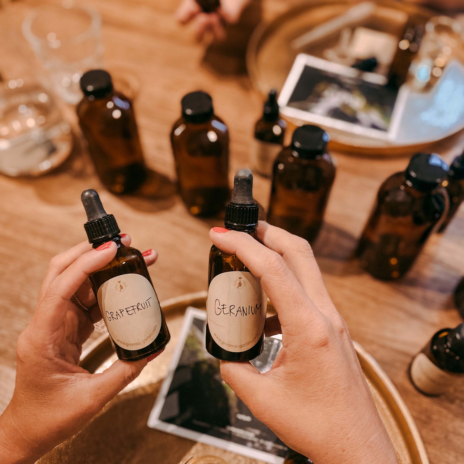 Zwei Hände halten Fläschchen mit Aufschrift „Grapefruit“ und „Geranium“ – ätherische öle workshop, bio facial serum, naturkosmetik diy.