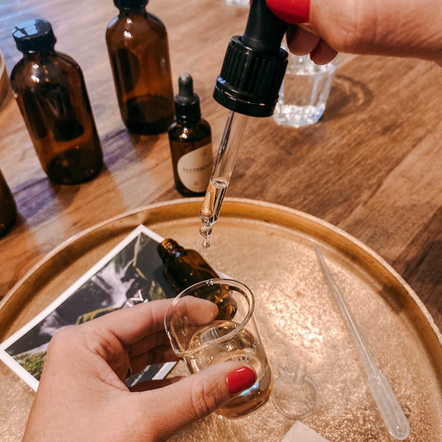 Pipette tropft Flüssigkeit in Glas, Flaschen im Hintergrund – bio facial serum, diy naturkosmetik, ätherische öle workshop.