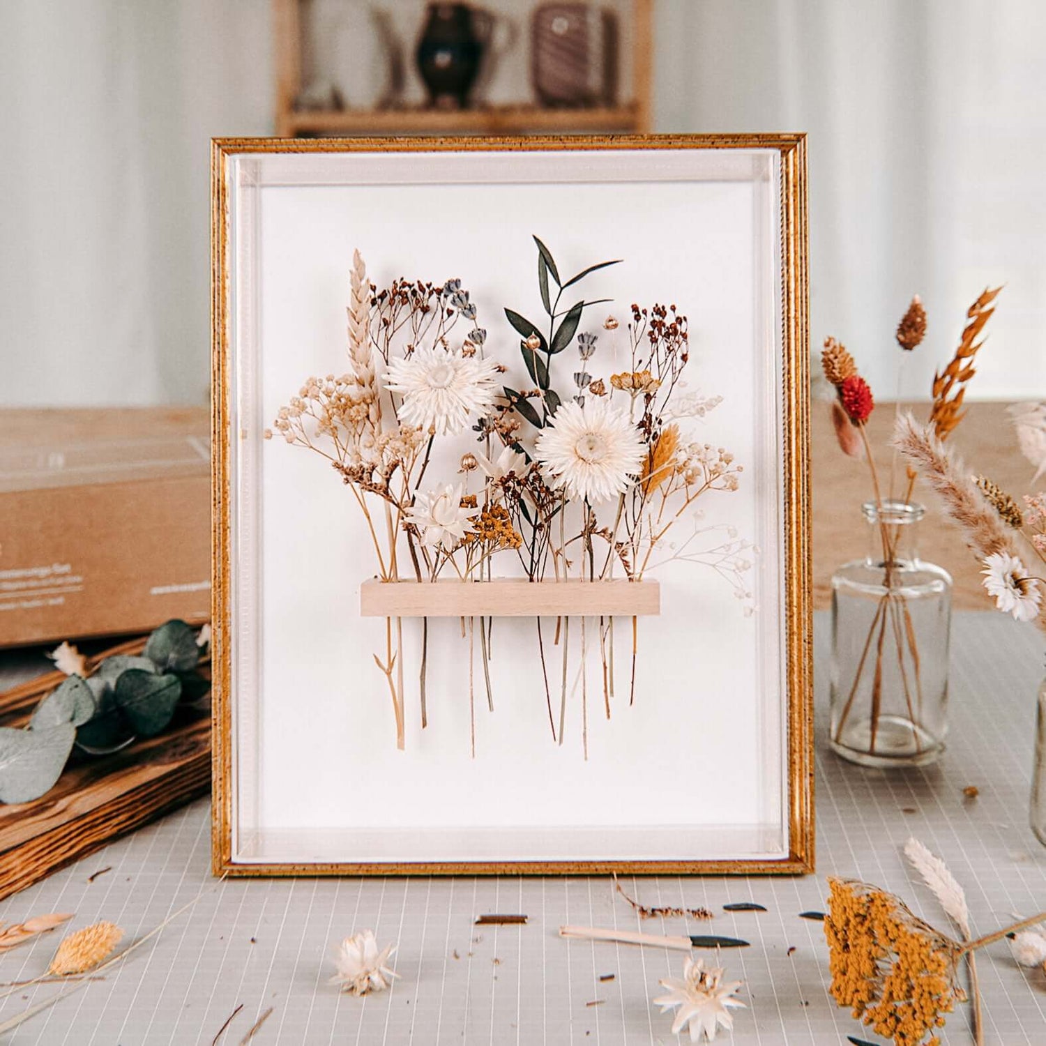 Goldener Rahmen mit weiß-beigen Blumen, Materialien liegen auf Tisch – trockenblumen kunstwerk workshop.