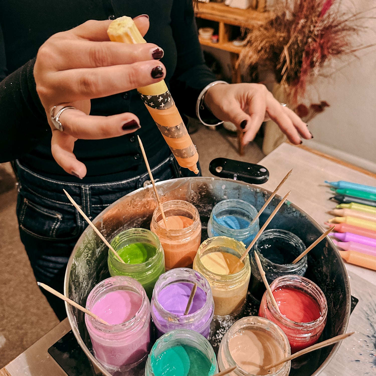 Topf mit geschmolzenem buntem Wachs, Hand dippt Kerze in Orange – Dip-Dye Technik.