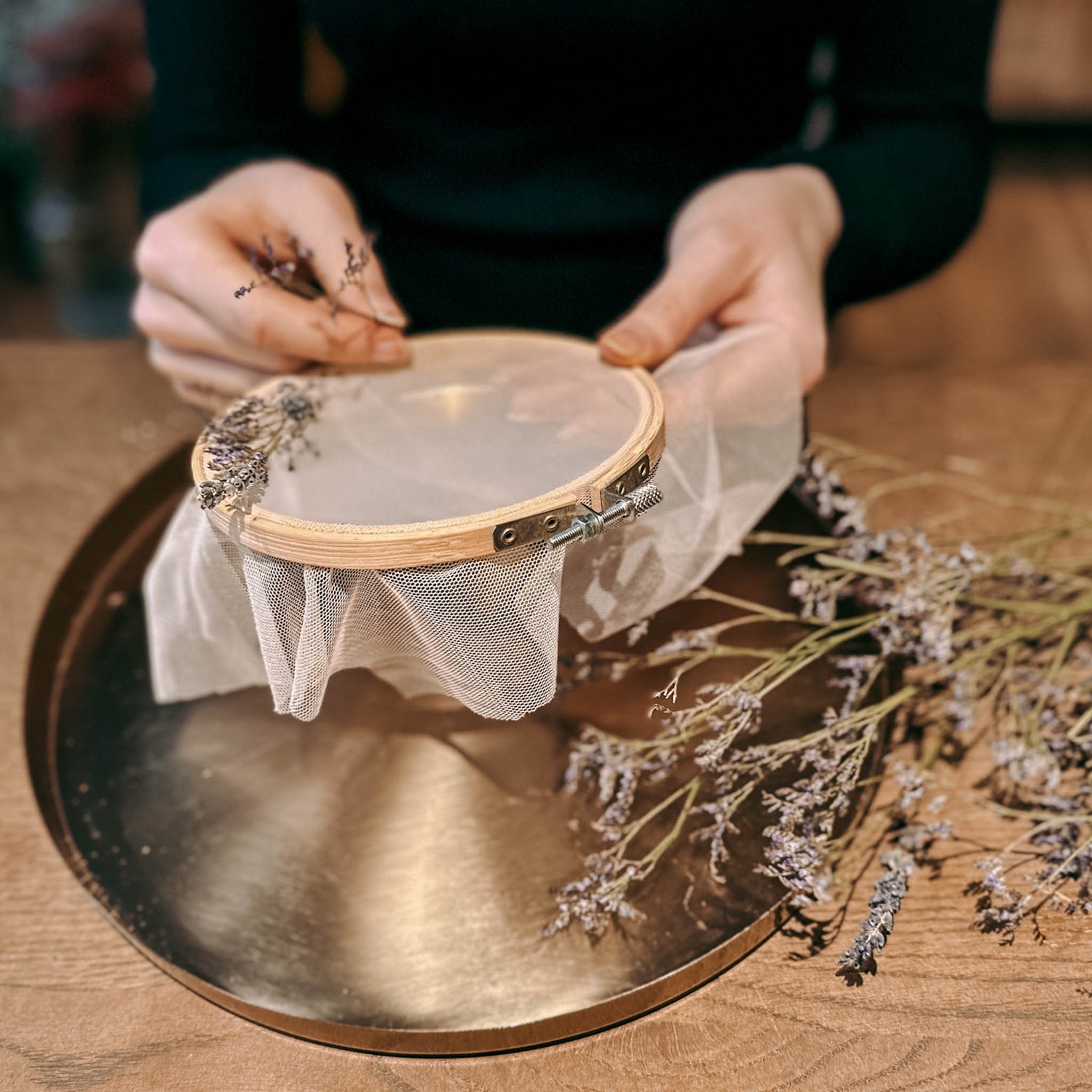 Zwei Hände halten halbfertigen Blumenring auf goldenem Tablett – DIY Trockenblumenring, florales Kunstwerk
