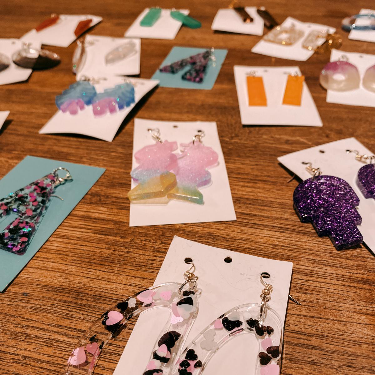 Viele bunte Resin Ohrringe in verschiedenen Formen auf Tisch – Resin Schmuck Workshop für Einsteiger.