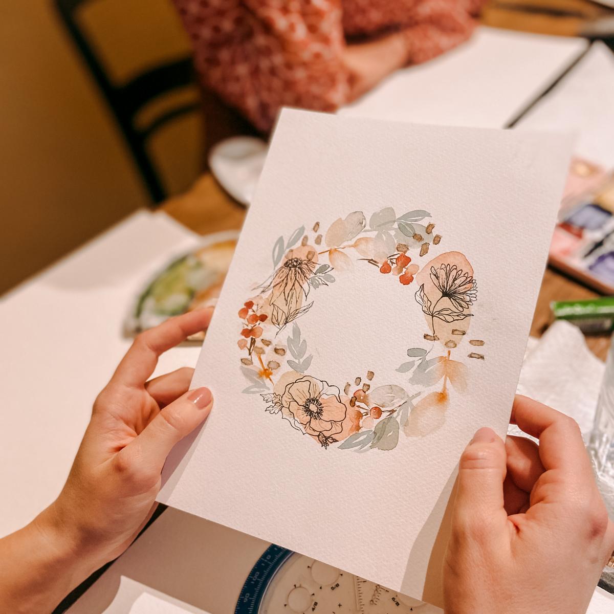 Zwei Hände halten Karte mit gemaltem Weihnachtskranz – Aquarell, Watercolour, DIY Karten, auch für Firmenevents.