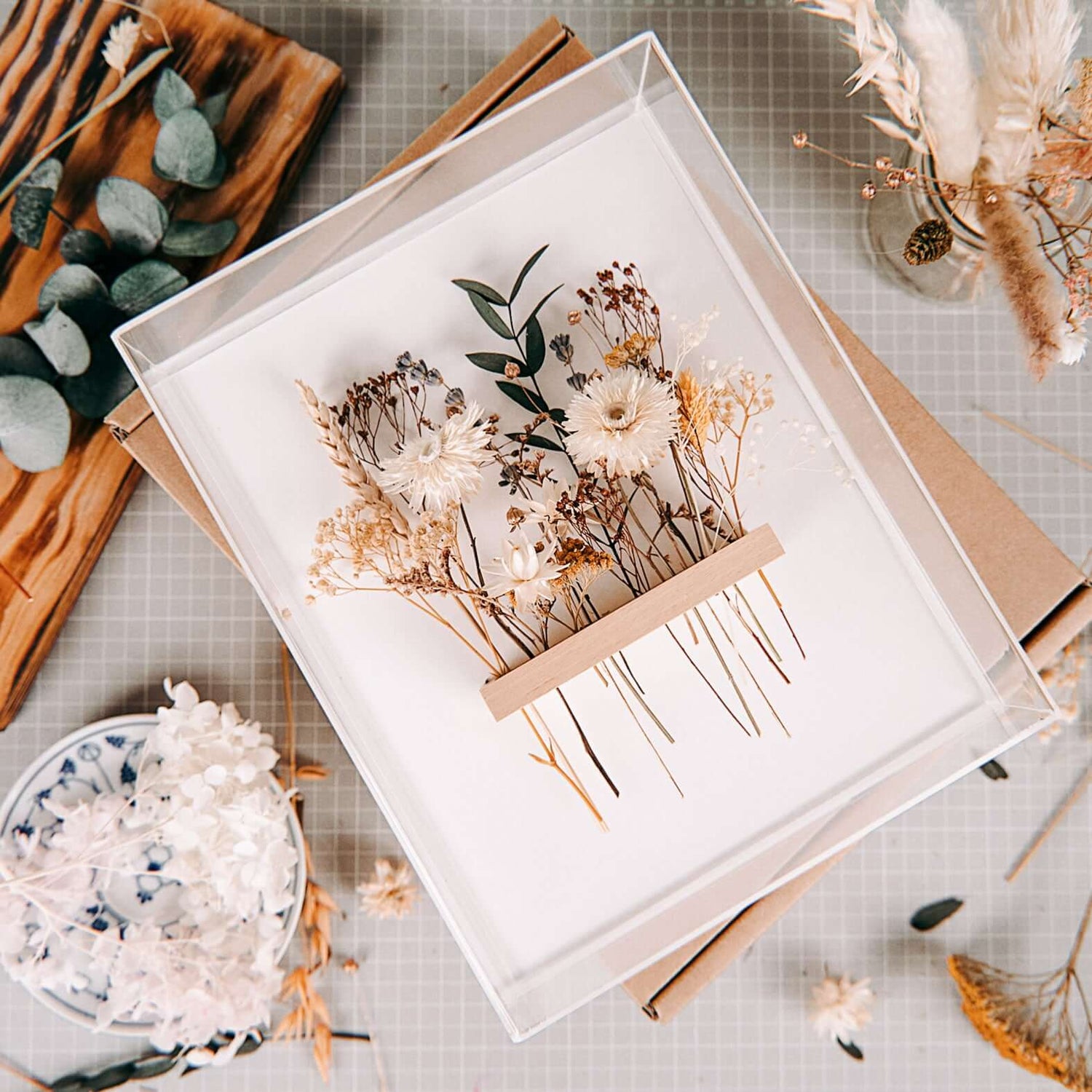 Fertiger Rahmen mit weißen und orangenen Blumen, Materialien liegen drumherum – trockenblumen kunstwerk workshop.