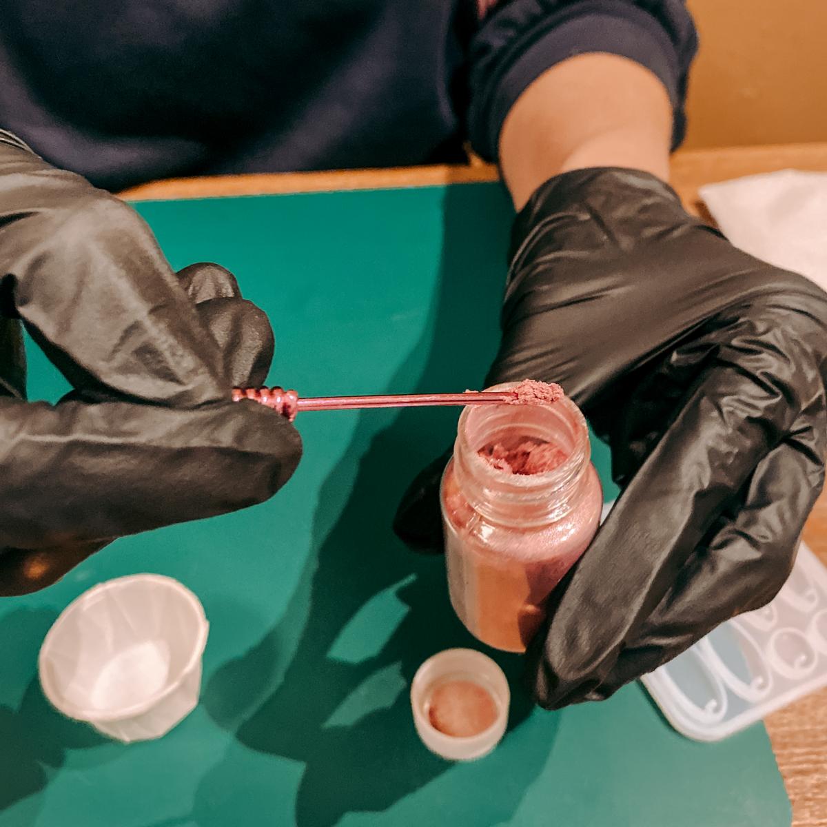 Hand mit Handschuhen trägt Glitzer auf – Epoxidharz Schmuck herstellen im kreativen Resin Workshop.