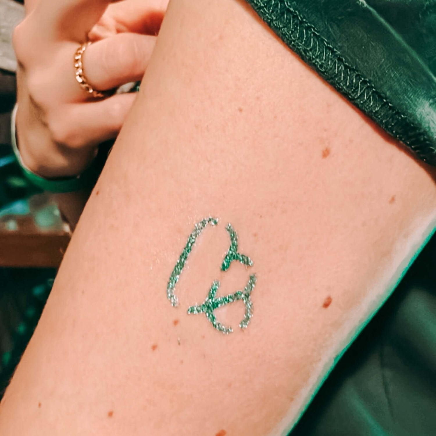 Nahaufnahme eines grünen Firmenlogo-Glitzertattoos – individuelles Teamevent Tattoo.