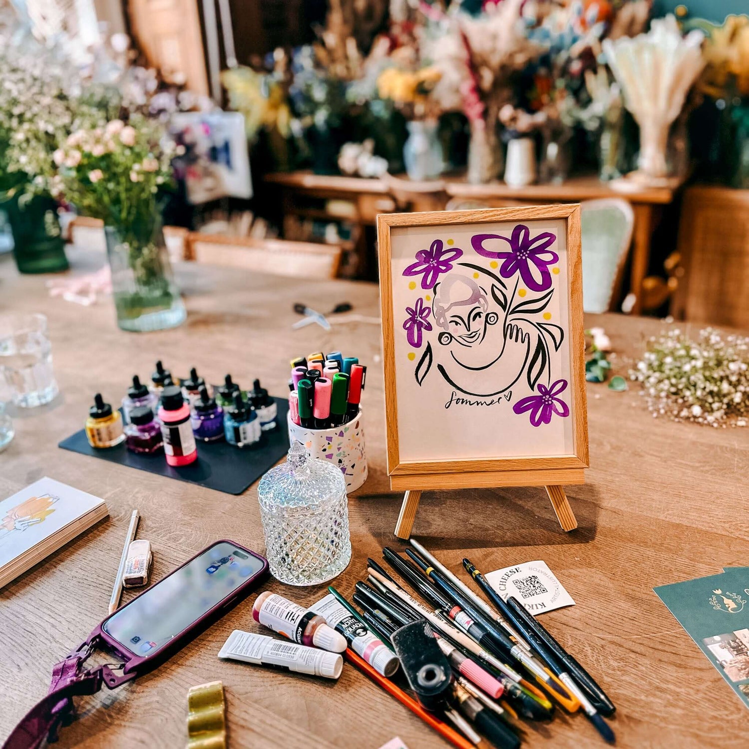 Fertiges lila Portrait im Rahmen mit Stiften und Pinseln auf Tisch – kreative Kundenaktion oder Firmenevent.