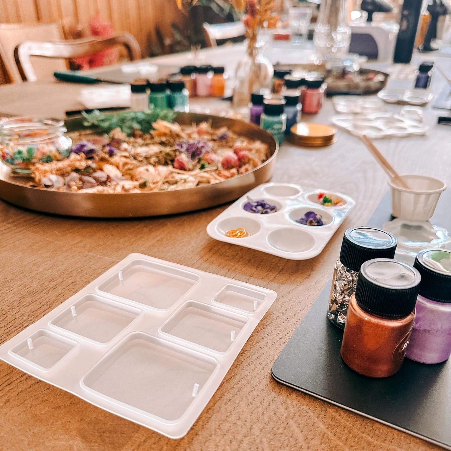 Viele Materialien und Gussformen mit Trockenblumen auf Holztisch – resin workshop, diy schmuck, auch für Firmenevents.