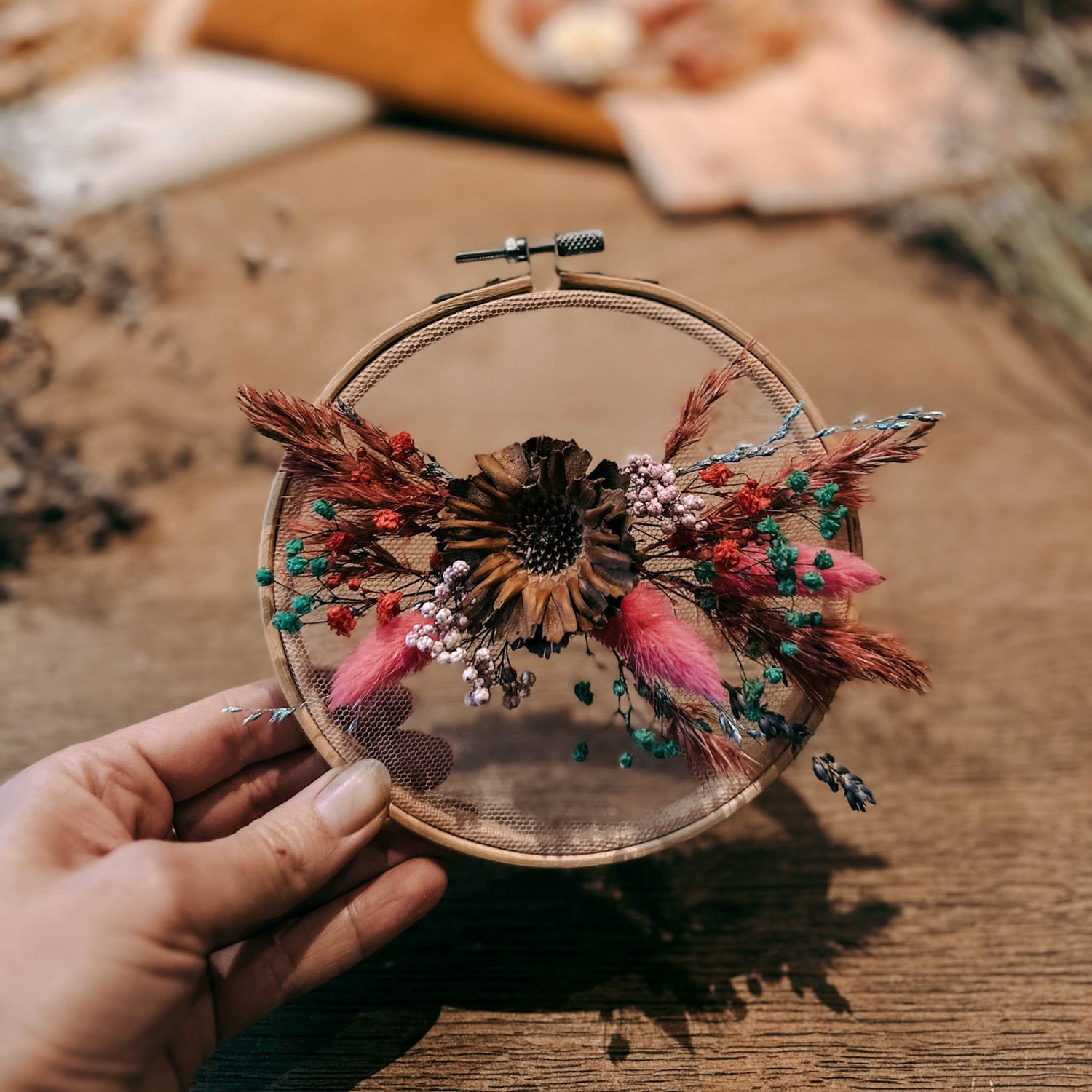 Hand hält fertiges Blumenwandbild mit pinken, blauen und roten Trockenblumen – florales Kunstwerk DIY