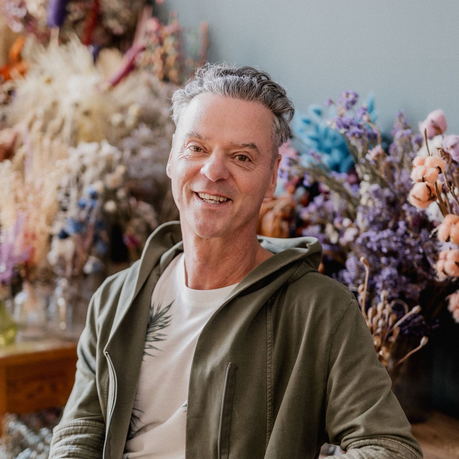 Mann lächelt in die Kamera, sitzt vor Blumen beim kreativen Workshop in Grimms Garten Berlin