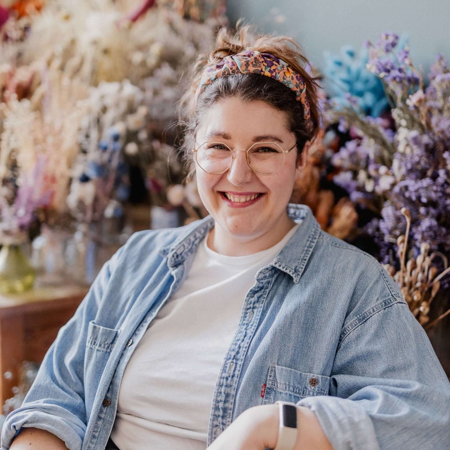 Frau mit Brille lächelt in die Kamera, sitzt vor Blumen beim kreativen Workshop in Grimms Garten Berlin