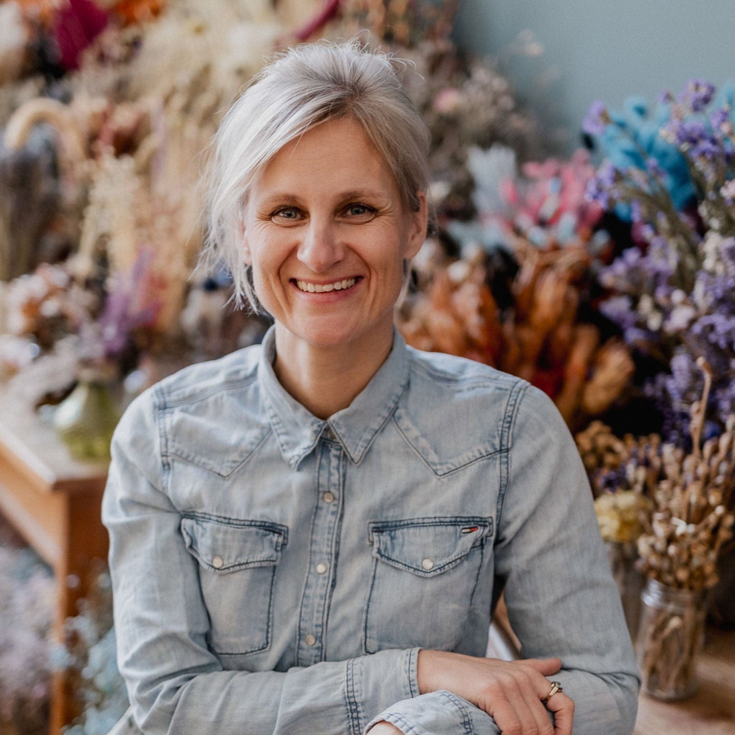 Frau im blauen Hemd sitzt lächelnd vor der Kamera, kreative Workshop-Atmosphäre bei Grimms Garten Berlin
