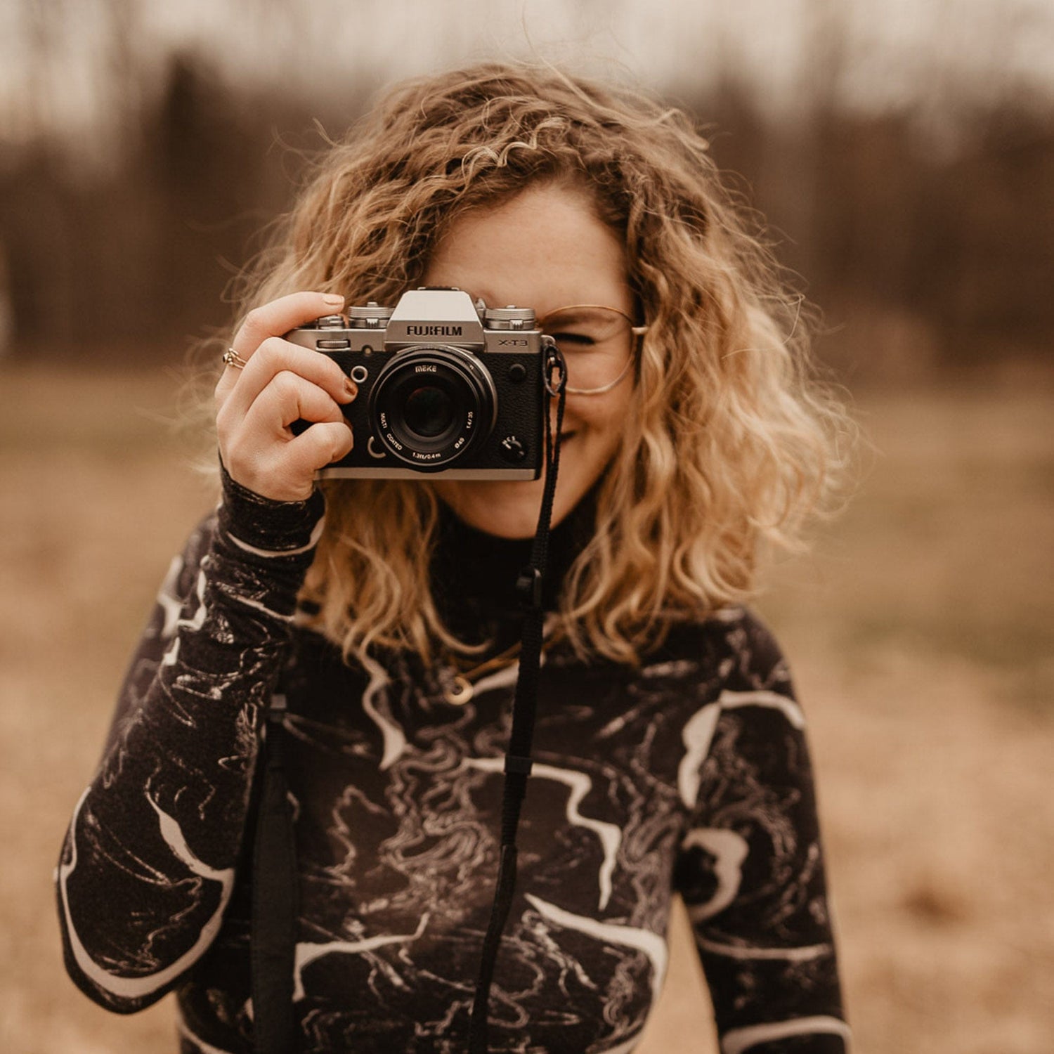 Frau hält Kamera vor Gesicht und lächelt, kreative Fotomomente beim Workshop in Grimms Garten Berlin