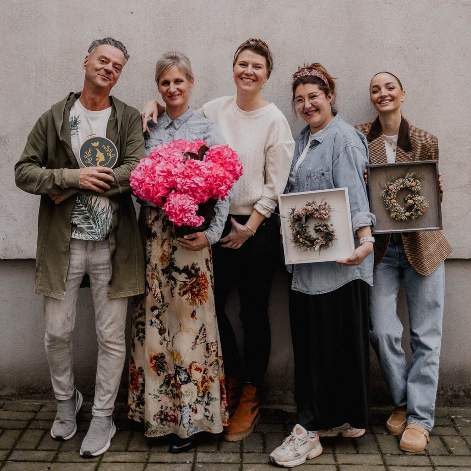 Fünf Personen halten Trockenblumen und Grimms Garten Logo vor Hauswand, kreative Workshop-Gruppe in Berlin