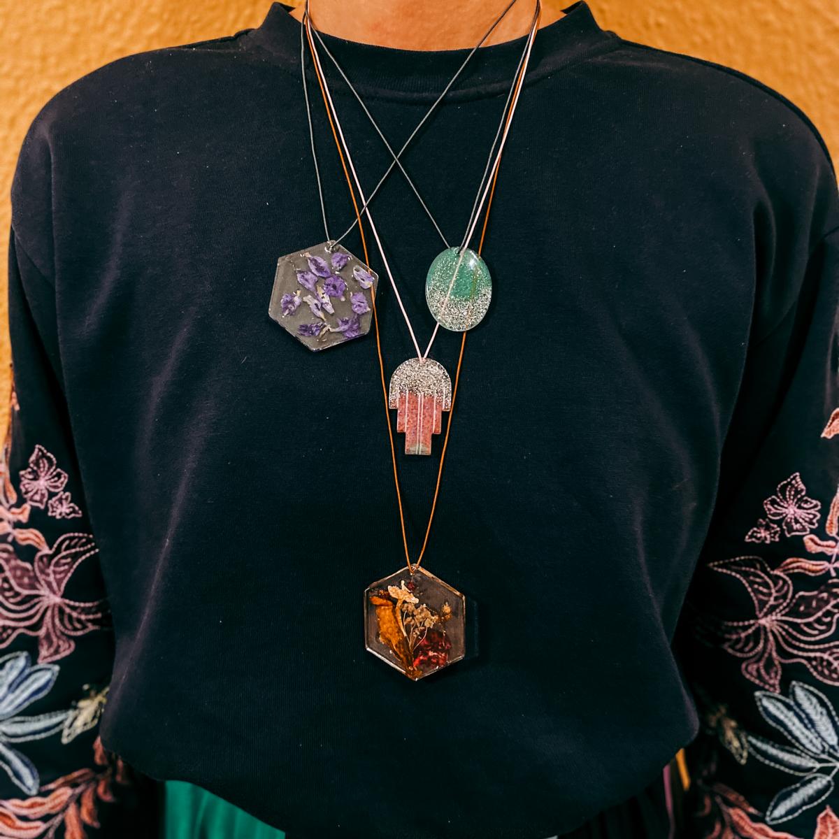 Person trägt vier Ketten mit Resin Anhängern in bunten Farben – DIY Epoxidharz Schmuckdesign.