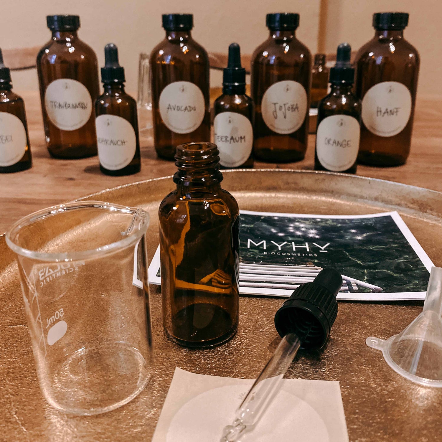 Goldenes Tablett mit Materialien und Flaschen im Hintergrund – naturkosmetik workshop, bio facial serum, diy hautpflege.