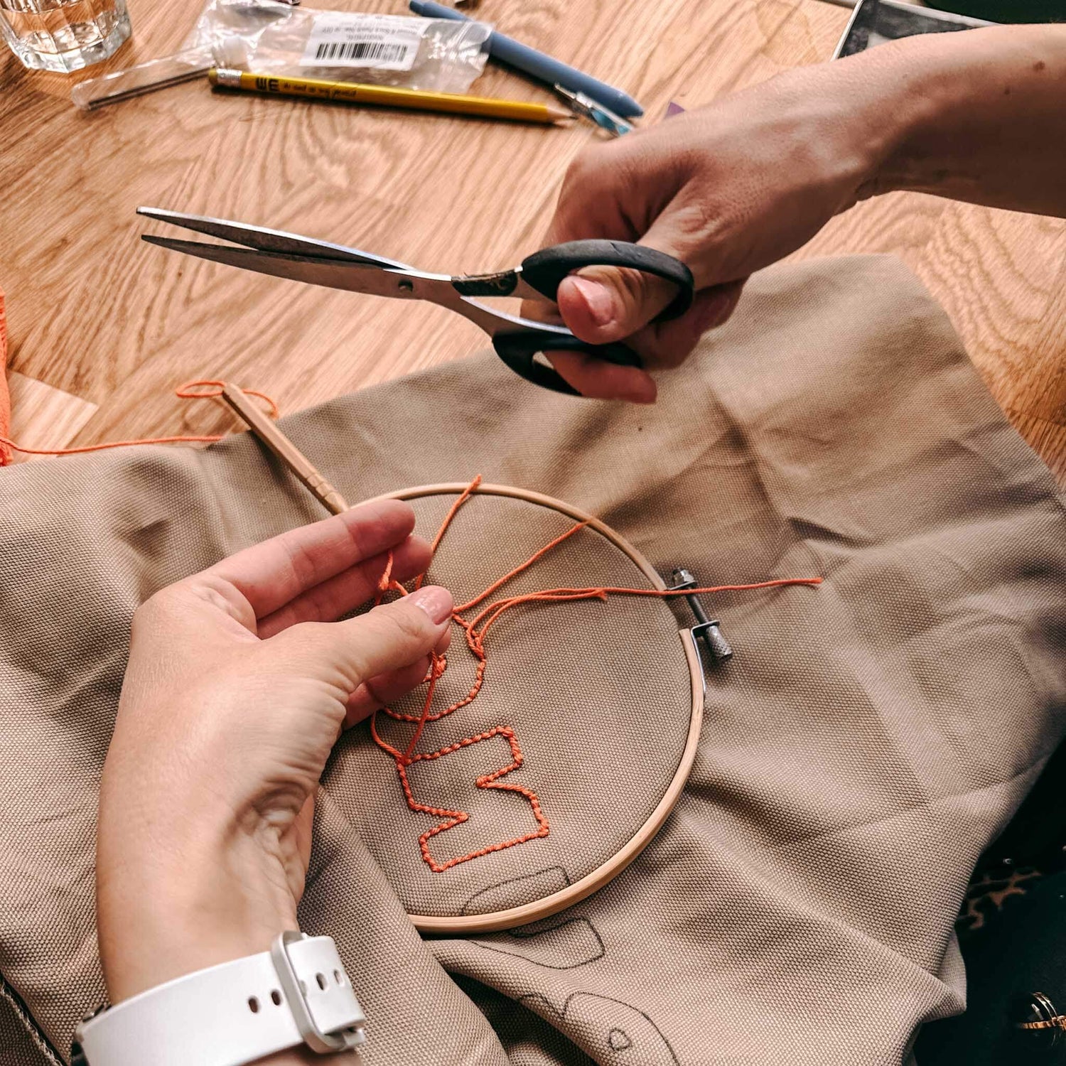 Zwei Hände bearbeiten Stoff mit Schere und orangener Wolle – Punch-Needle Workshop Berlin.