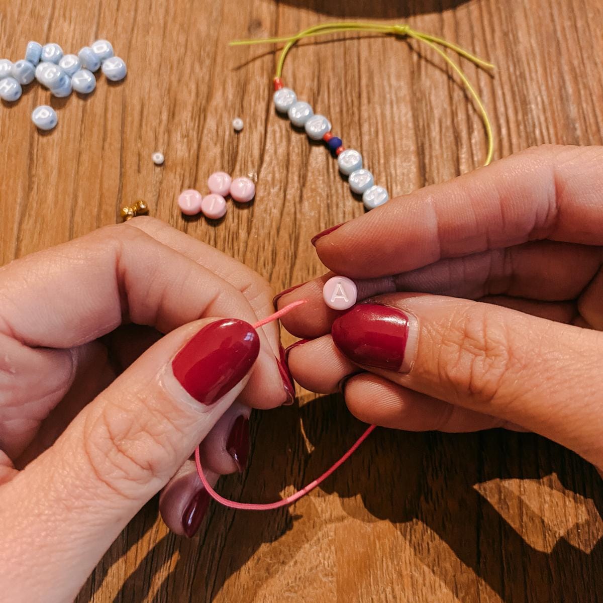 Zwei Hände fädeln Buchstaben „A“ auf Schnur – DIY Perlenschmuck, Workshop Berlin, Armband selber machen.