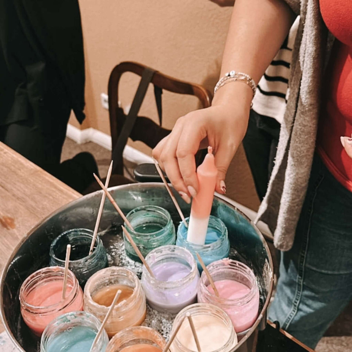 Hand taucht Kerze in buntes Wachs, daneben Gläser mit Wachs – dip dye kerzen, kerzen färben, buntkerzen selber machen.Auch als Firmenevent buchbar.