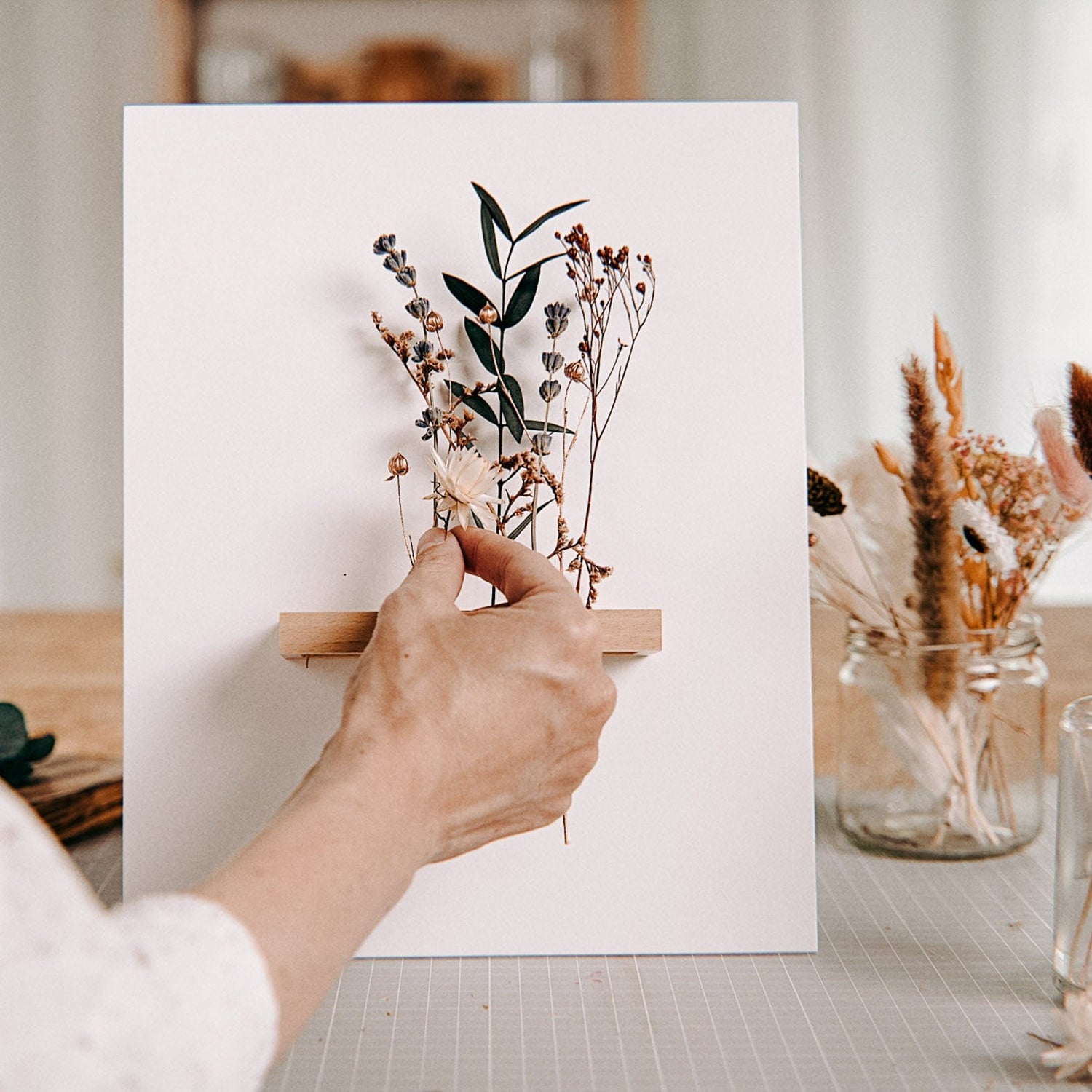 Hand steckt Blumen in Rahmen, nur Eukalyptus und weiße Blumen – trockenblumen kunstwerk workshop.