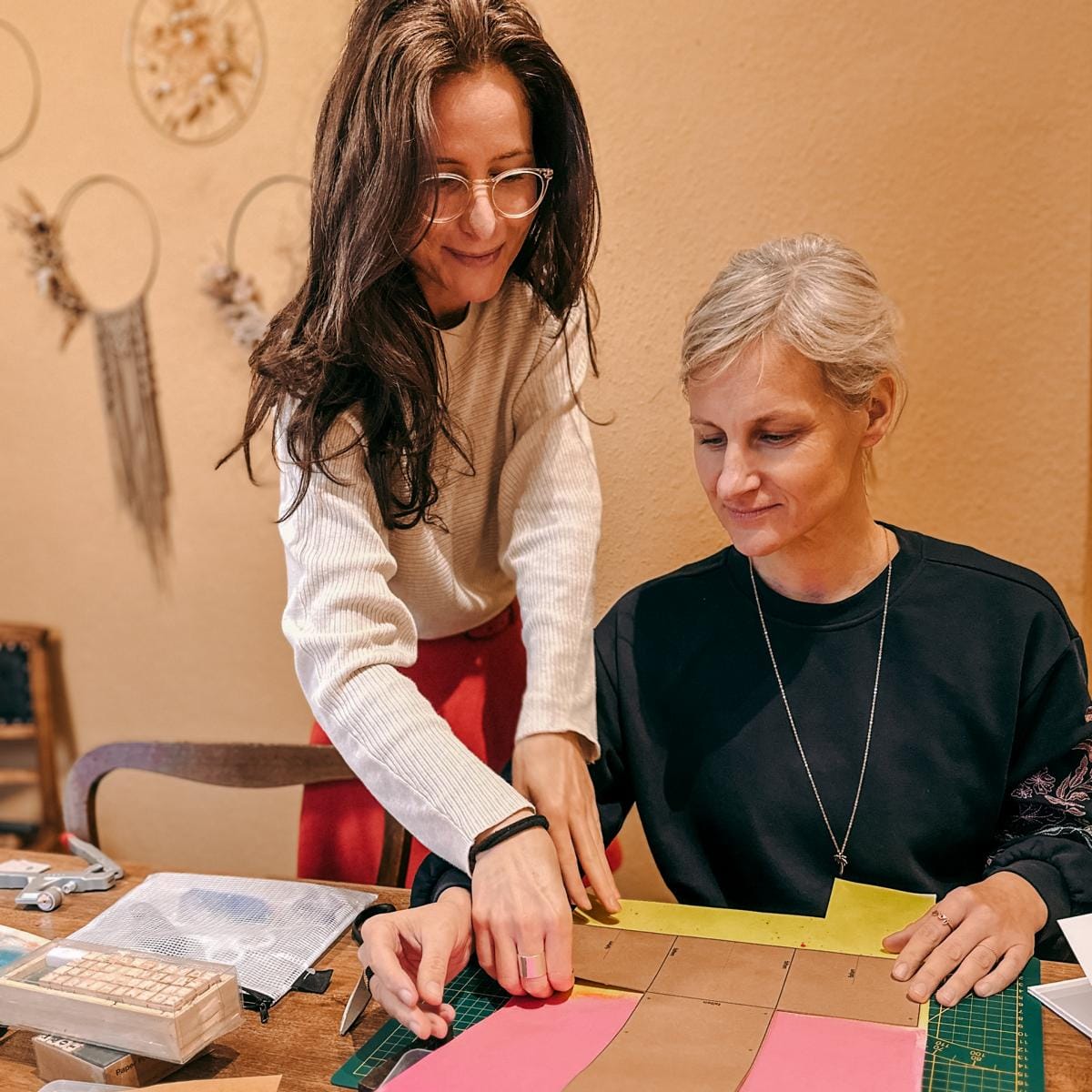 Kursleiter zeigt Teilnehmerin, wie man Leder zuschneidet, kreativer DIY Workshop bei Grimms Garten Berlin