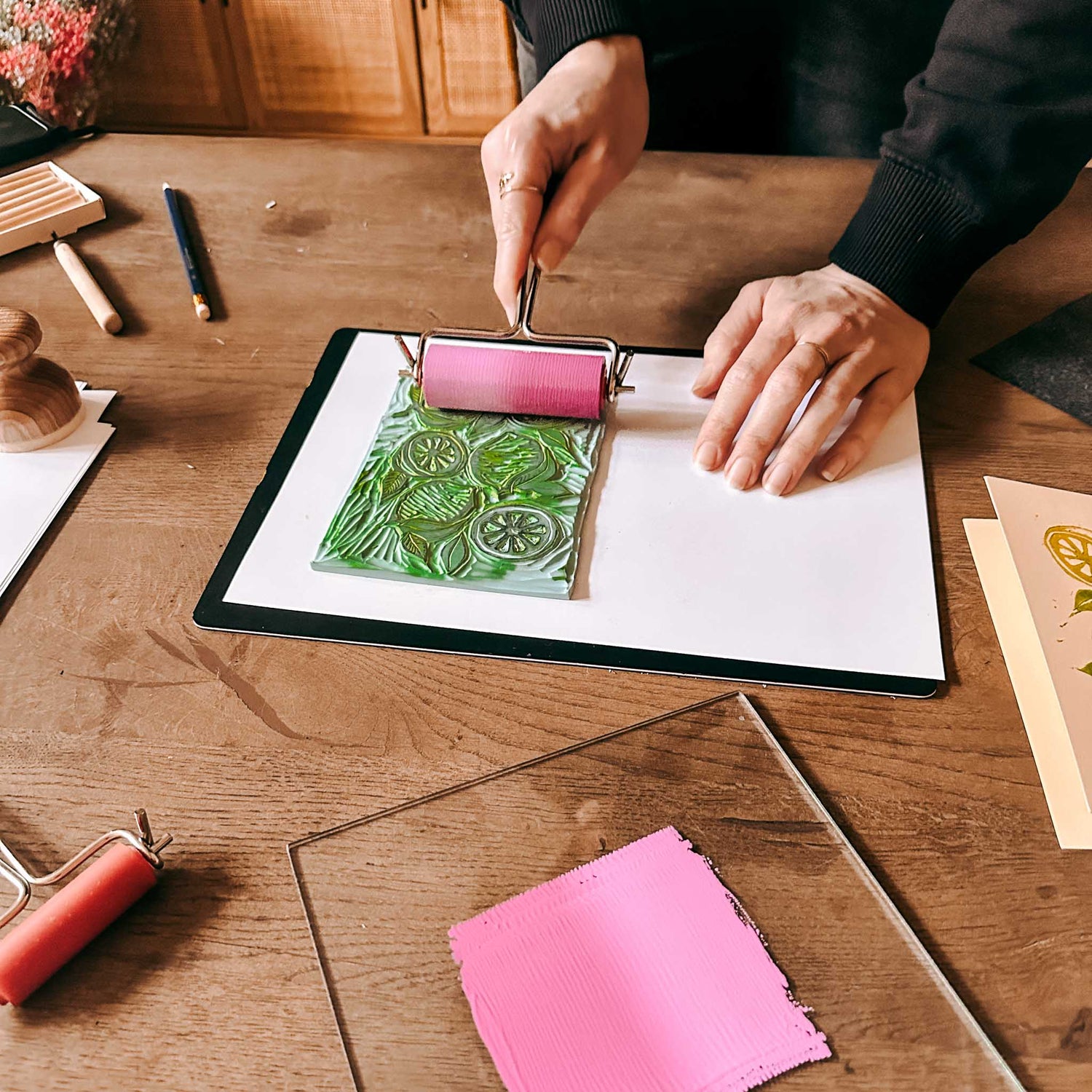 Pinke Rolle färbt grünen Zitronendruck auf großem Blatt, zwei Hände arbeiten – Linolschnitt, Linoldruck.