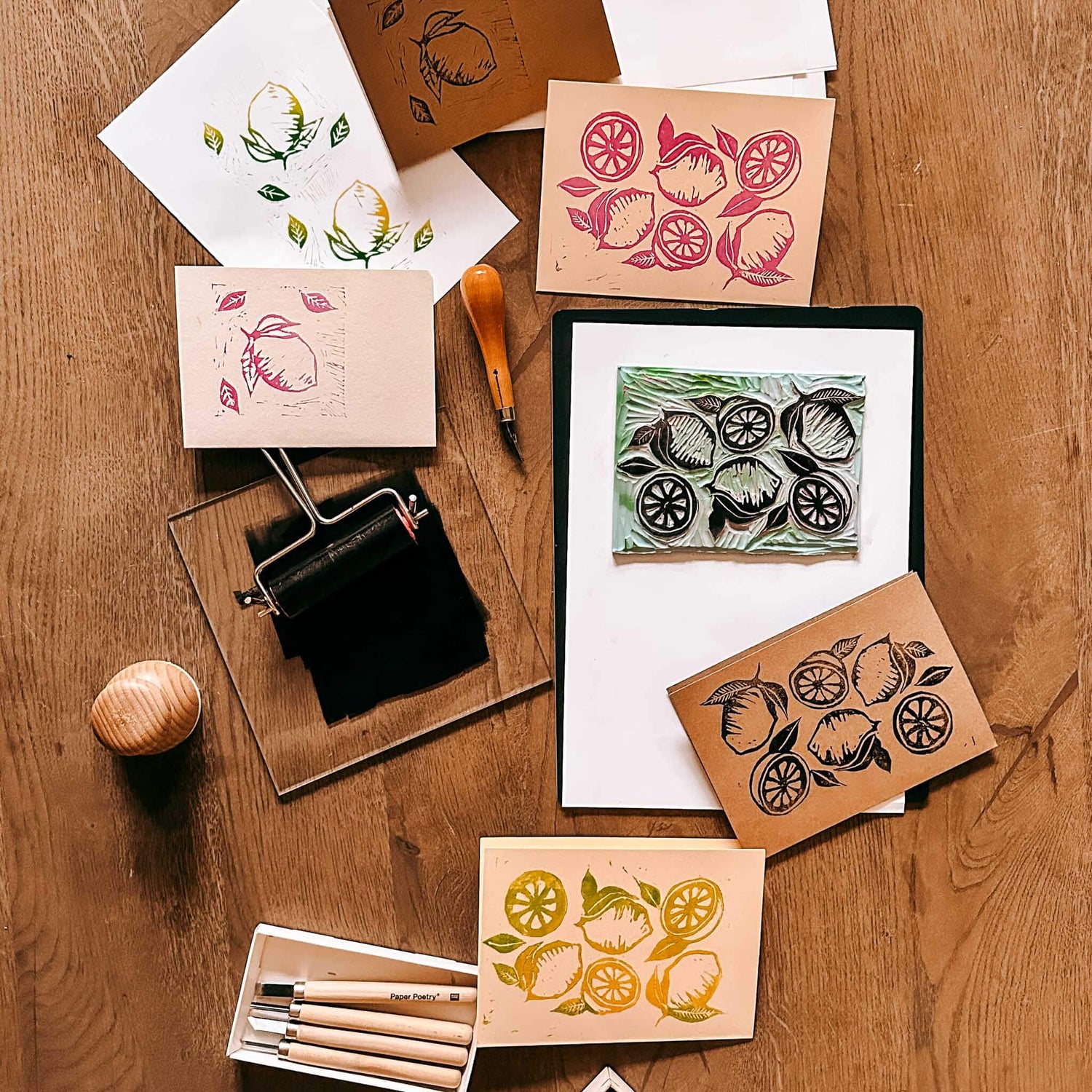 Mehrere Drucke mit verschiedenen Farben auf Tisch, schwarze Rolle und Farbe – Linolschnitt, Linoldruck.