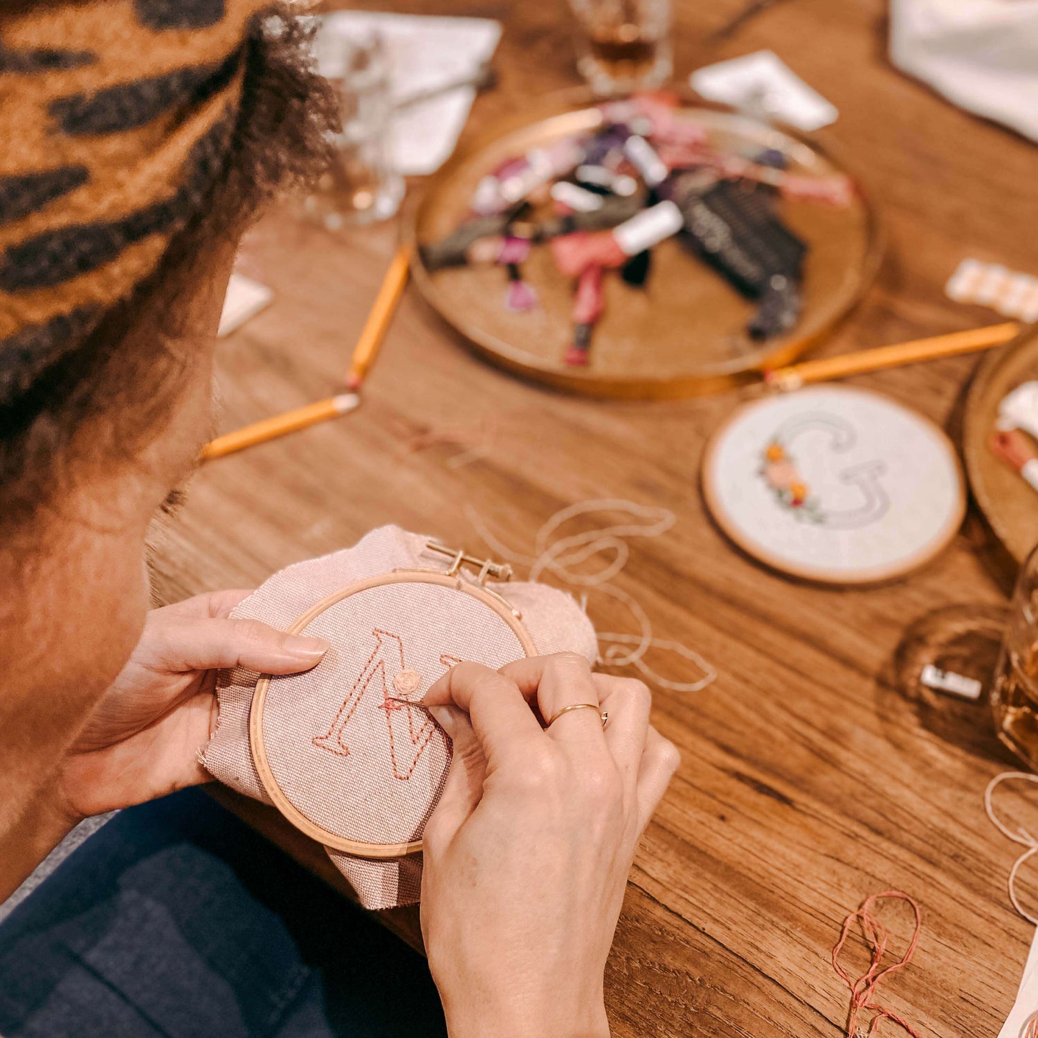 Person stickt Buchstabe N auf eingerahmtem Stoff – Stickerei Workshop, Monogramm Handarbeit
