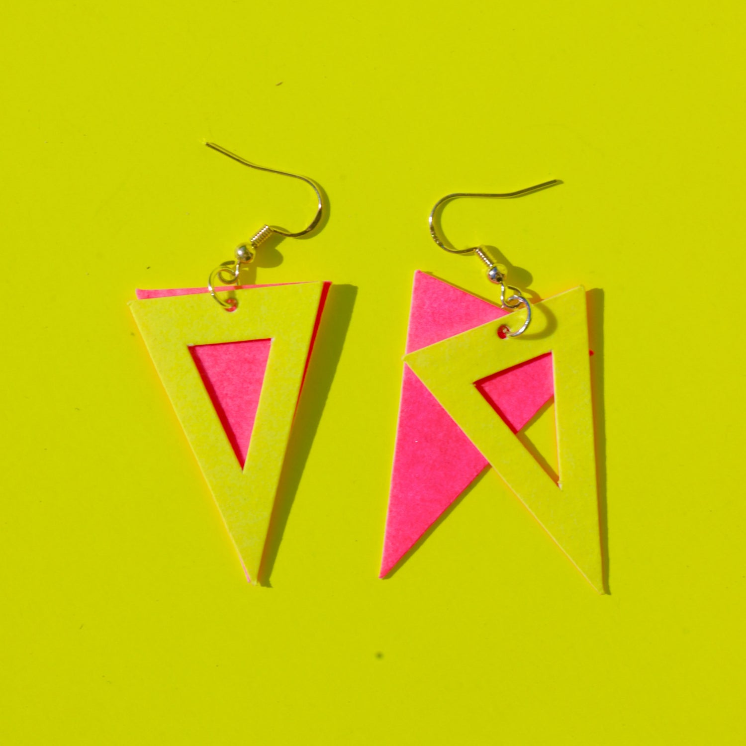 Dreiecksförmige Ohrringe aus veganem Leder in Pink und Gelb auf gelbem Hintergrund – DIY Schmuckdesign Kurs.