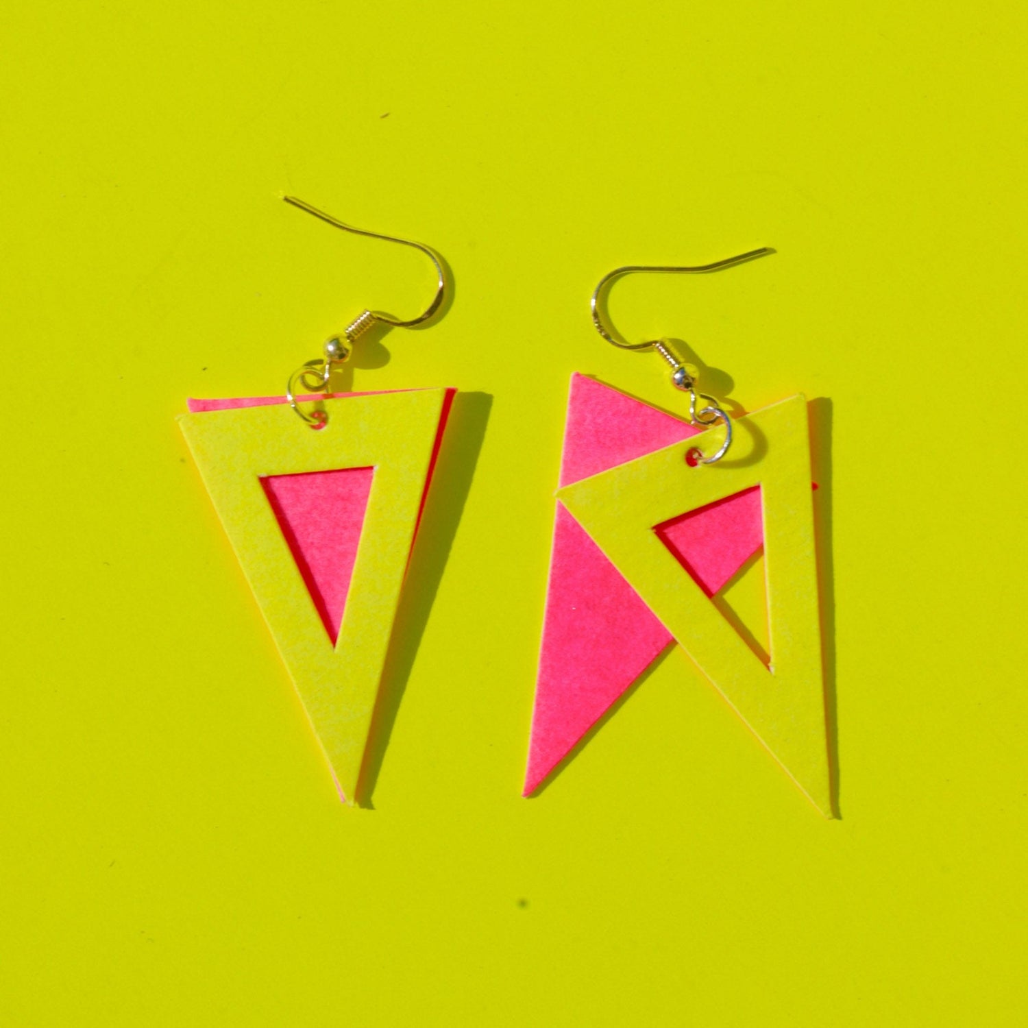 Dreiecksförmige Ohrringe aus veganem Leder in Pink und Gelb auf gelbem Hintergrund – DIY Schmuckdesign Kurs.