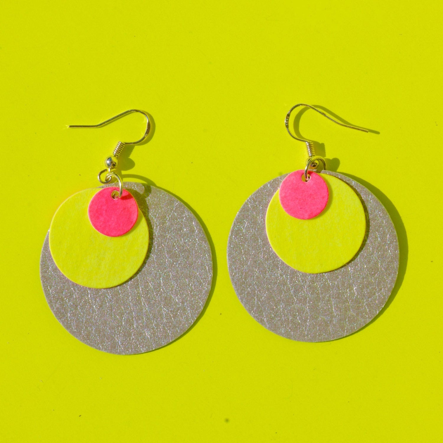 Runde Ohrringe aus veganem Leder in Gelb, Pink und Grau auf gelbem Hintergrund – nachhaltiger Schmuck Workshop