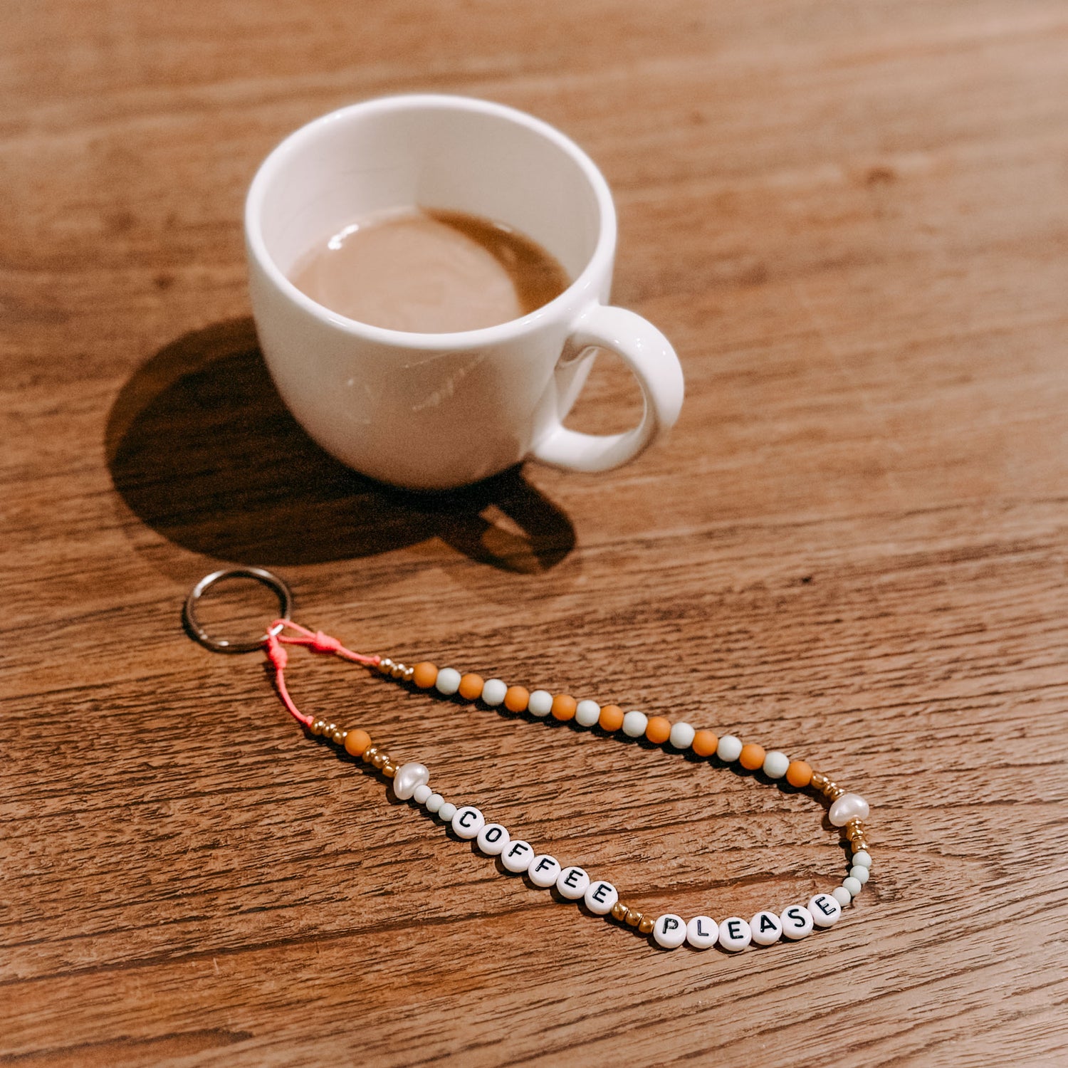 Kaffeetasse und Perlenschlüsselanhänger „Coffee please“ auf Tisch – DIY Schmuck, Perlenschmuck Workshop.