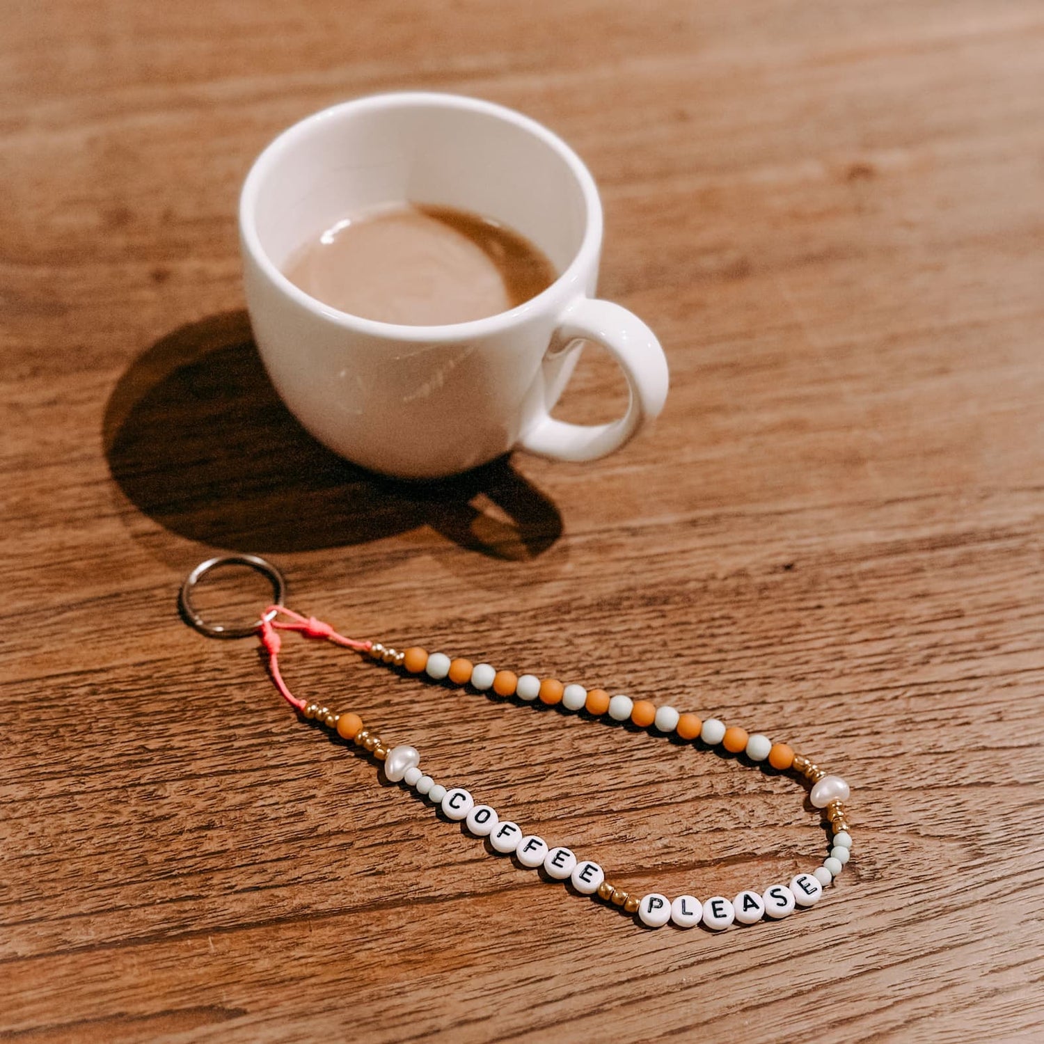 Kaffeetasse und Perlenschlüsselanhänger „Coffee please“ auf Tisch – DIY Schmuck, Perlenschmuck Workshop.