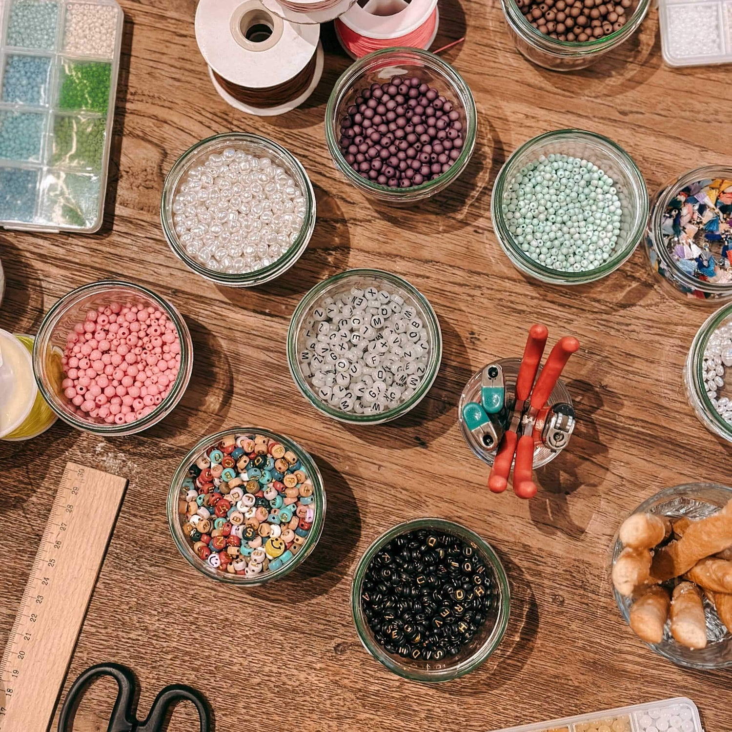 Viele verschiedene Perlen in Gläsern auf Holztisch verteilt, kreativer Schmuckworkshop bei Grimms Garten Berlin