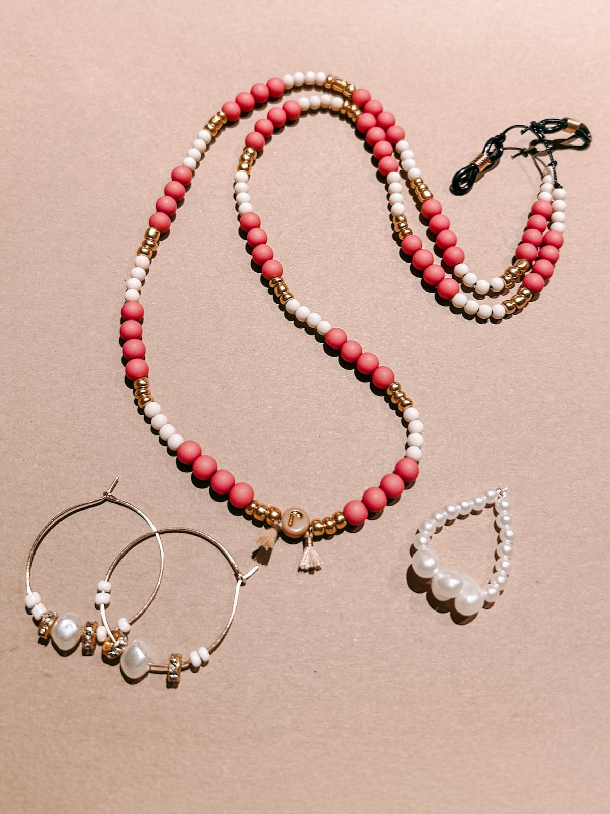 Brillenkette mit passenden Ohrringen und Perlenring auf farbigem Hintergrund fotografiert, Schmuckstücke aus dem DIY Perlenschmuck Workshop von GRIMMS GARTEN in Berlin