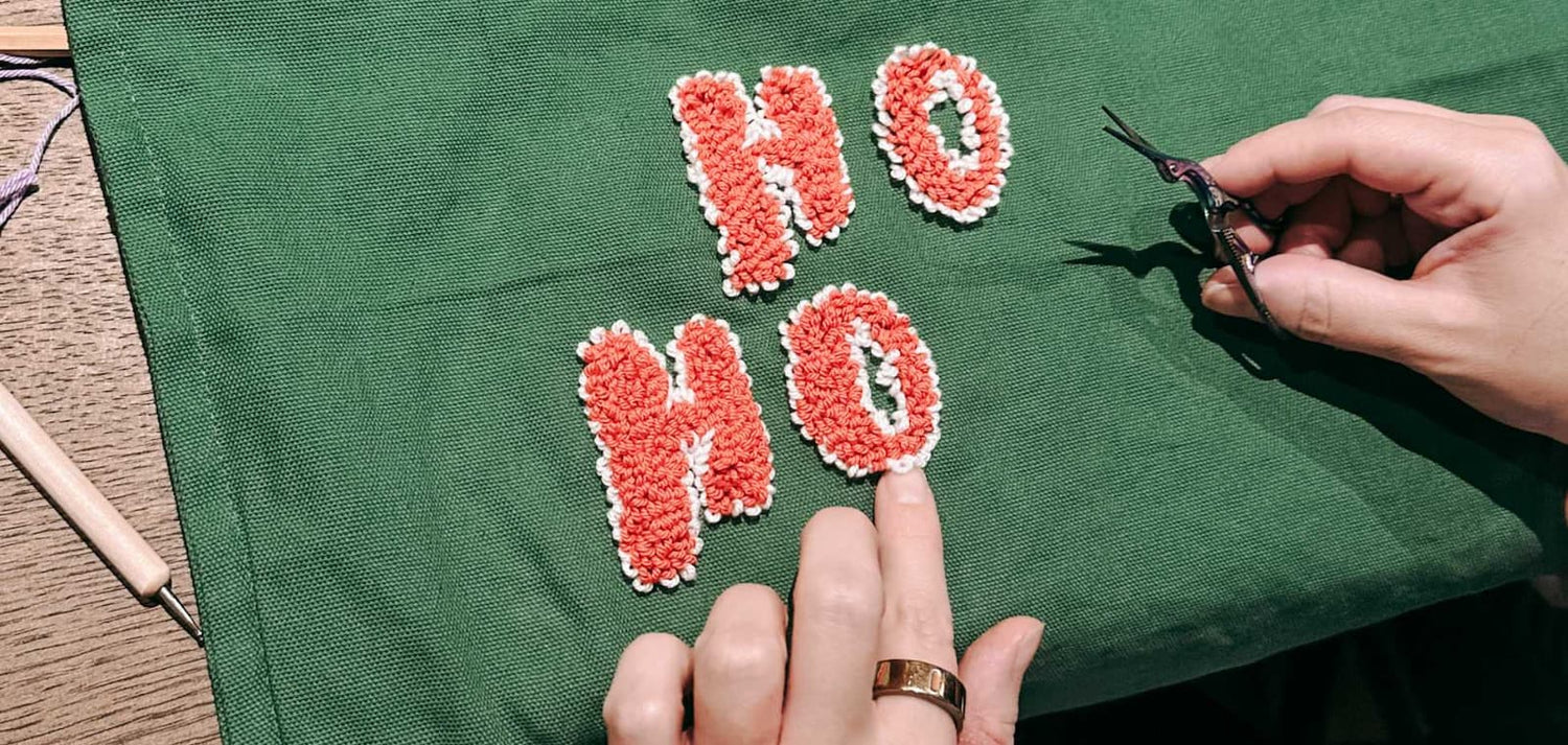 „Ho Ho“ wird auf grünem Stoff gepuncht – Punchneedle Workshop im GRIMMS GARTEN kreativ erleben.