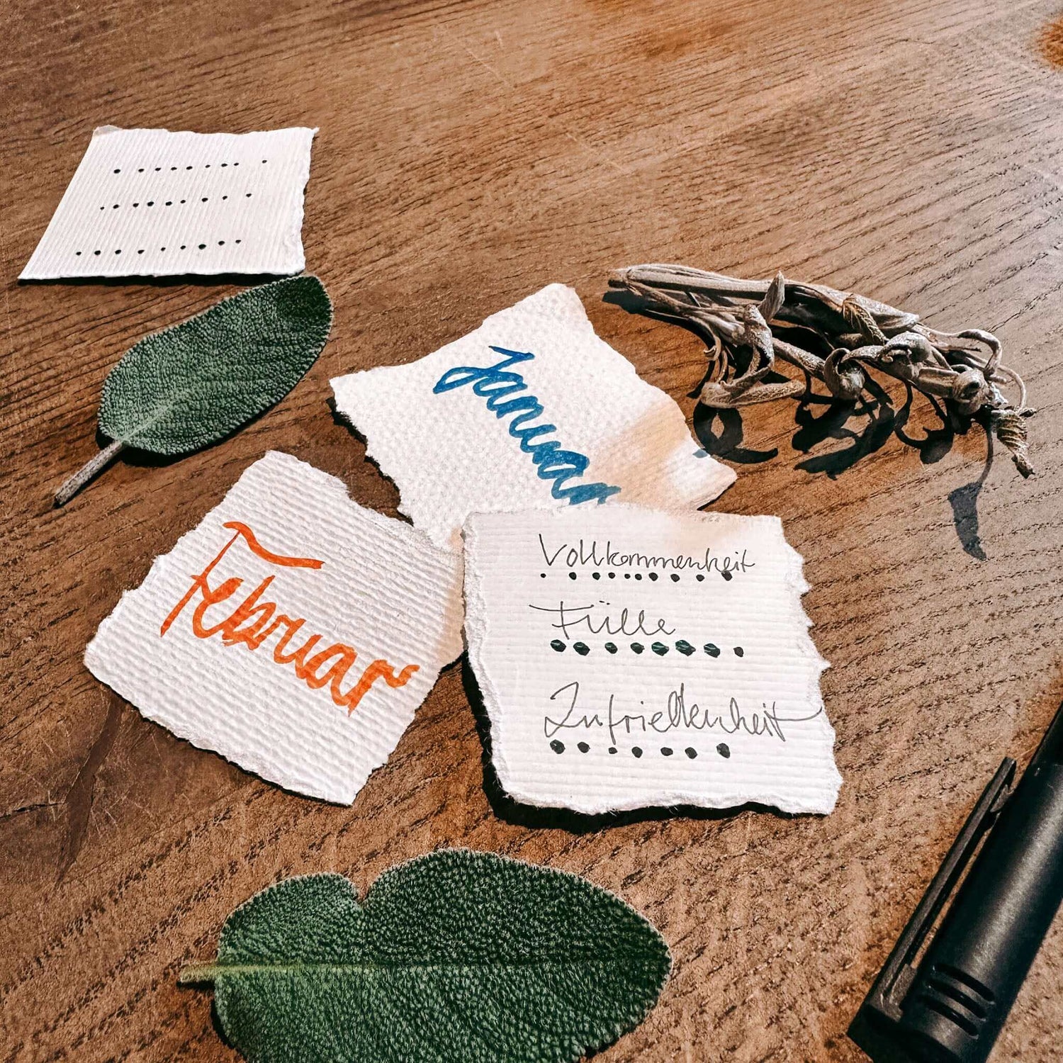 Mehrere Zettel mit zwei Kräuterblättern auf Tisch – rauhnächte workshop, achtsamkeit, spiritual workshop berlin.