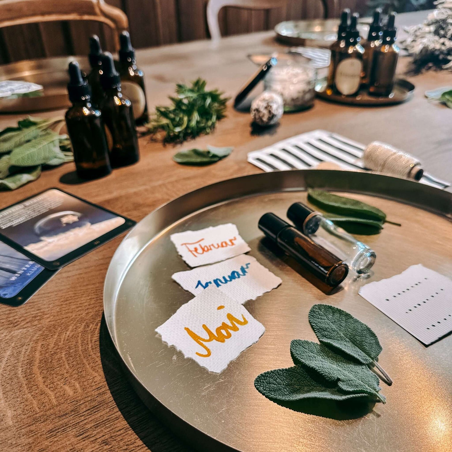 Drei Zettel mit „Mai“, „Januar“ und „Februar“ neben Blättern und Fläschchen auf goldenem Tablett – rauhnacht ritual, rauhnächte workshop, diy ritualset.