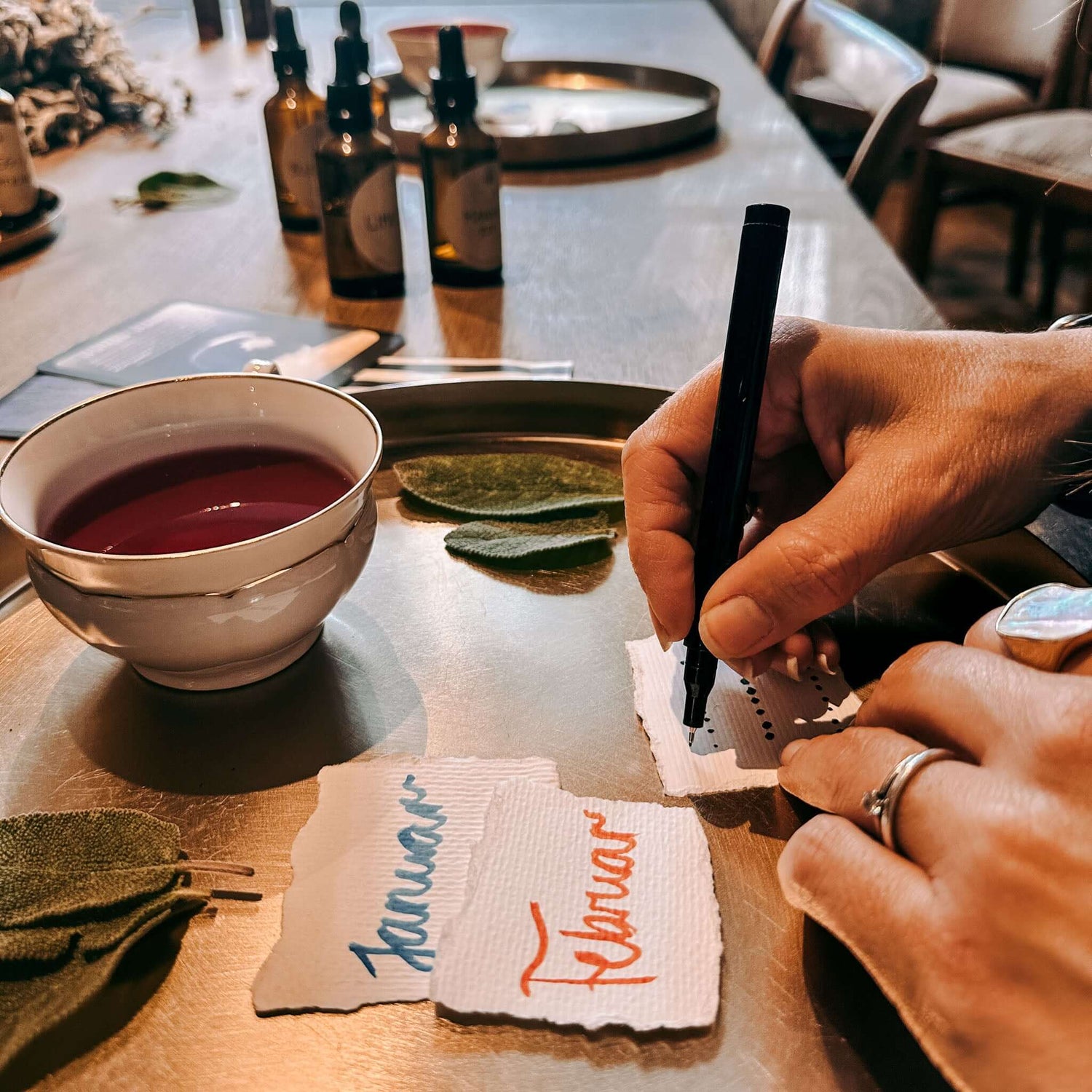 Hand schreibt auf feinen Zettel, daneben weitere Zettel, Tasse und Blätter auf goldenem Tablett – rauhnächte workshop, achtsamkeit, ritual set.