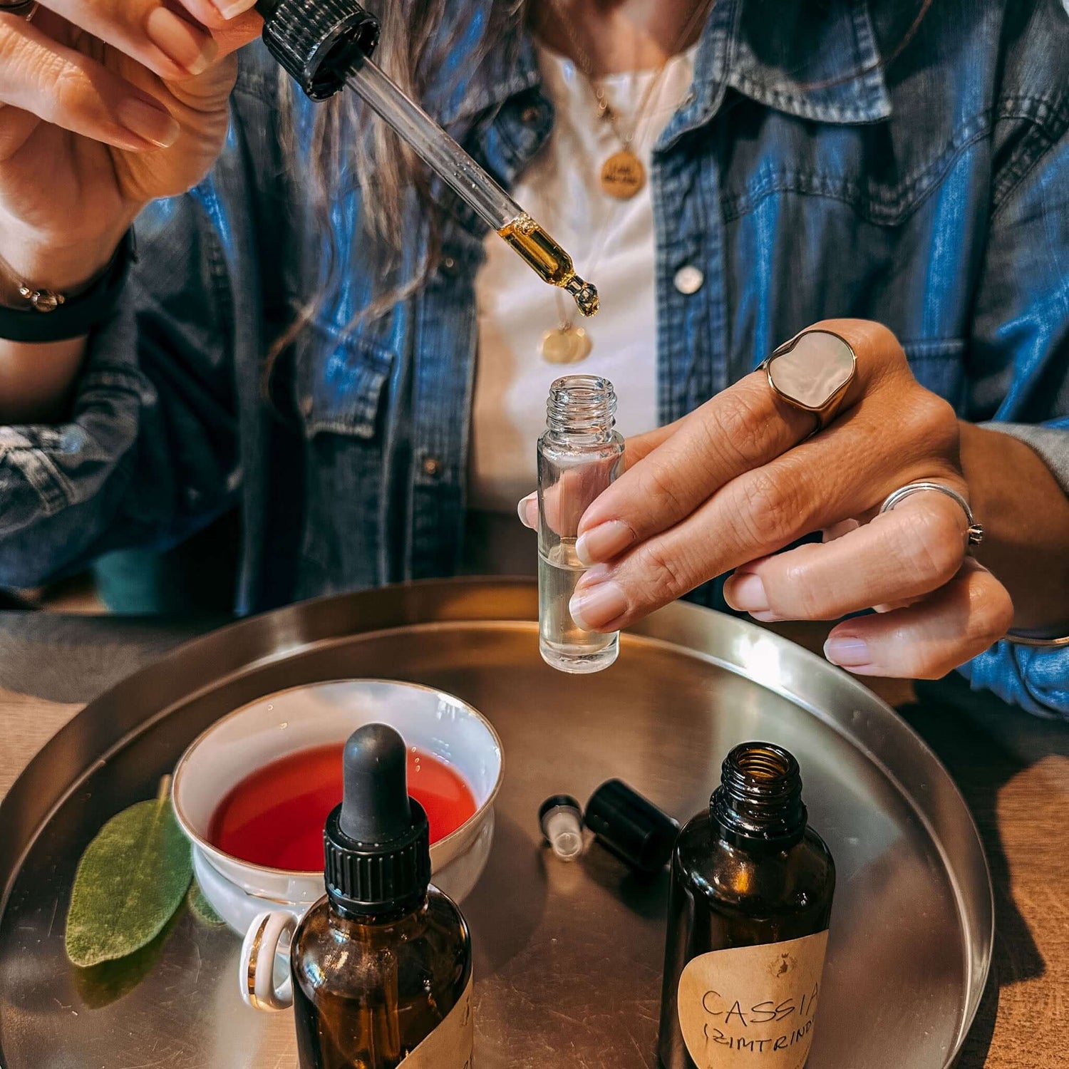 Hände tropfen Öl in kleinen Behälter, daneben Tasse und Ölmischung auf goldenem Tablett – ätherische öle, rauhnacht ritual, rauhnächte workshop.