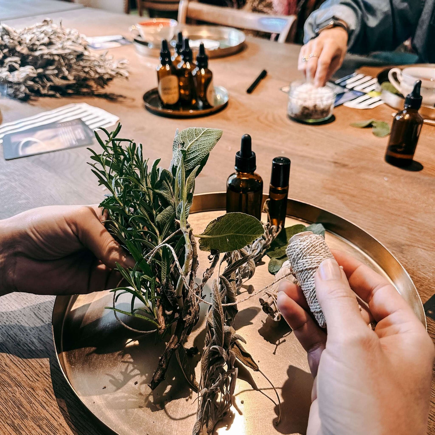 Hände wickeln Kordel um getrocknete Kräuter zu Räucherbündel – räucherkräuter, diy ritualset, rauhnacht ritual.