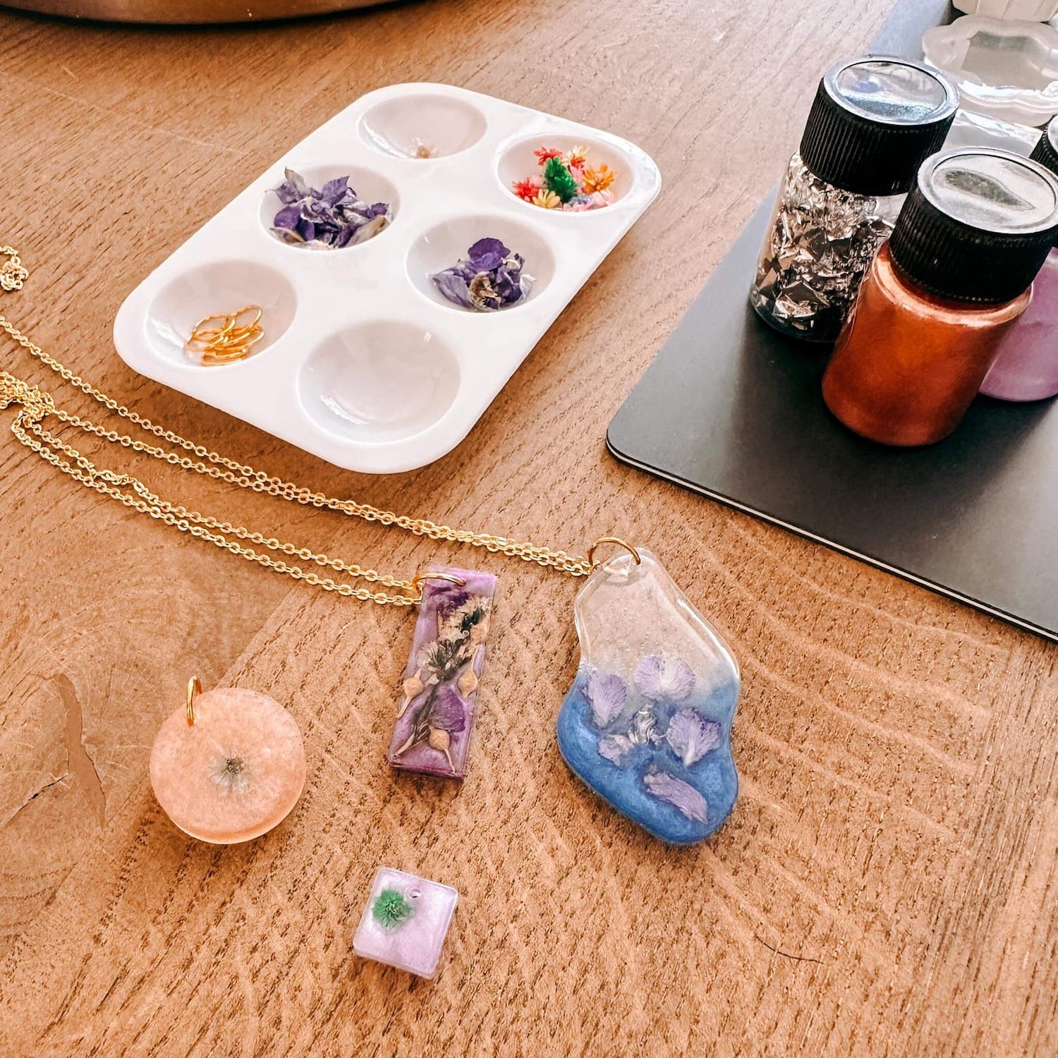 Blumenpalette mit Resin-Anhängern auf Holztisch – resin schmuck workshop, uv harz schmuck, auch für Firmenevents.