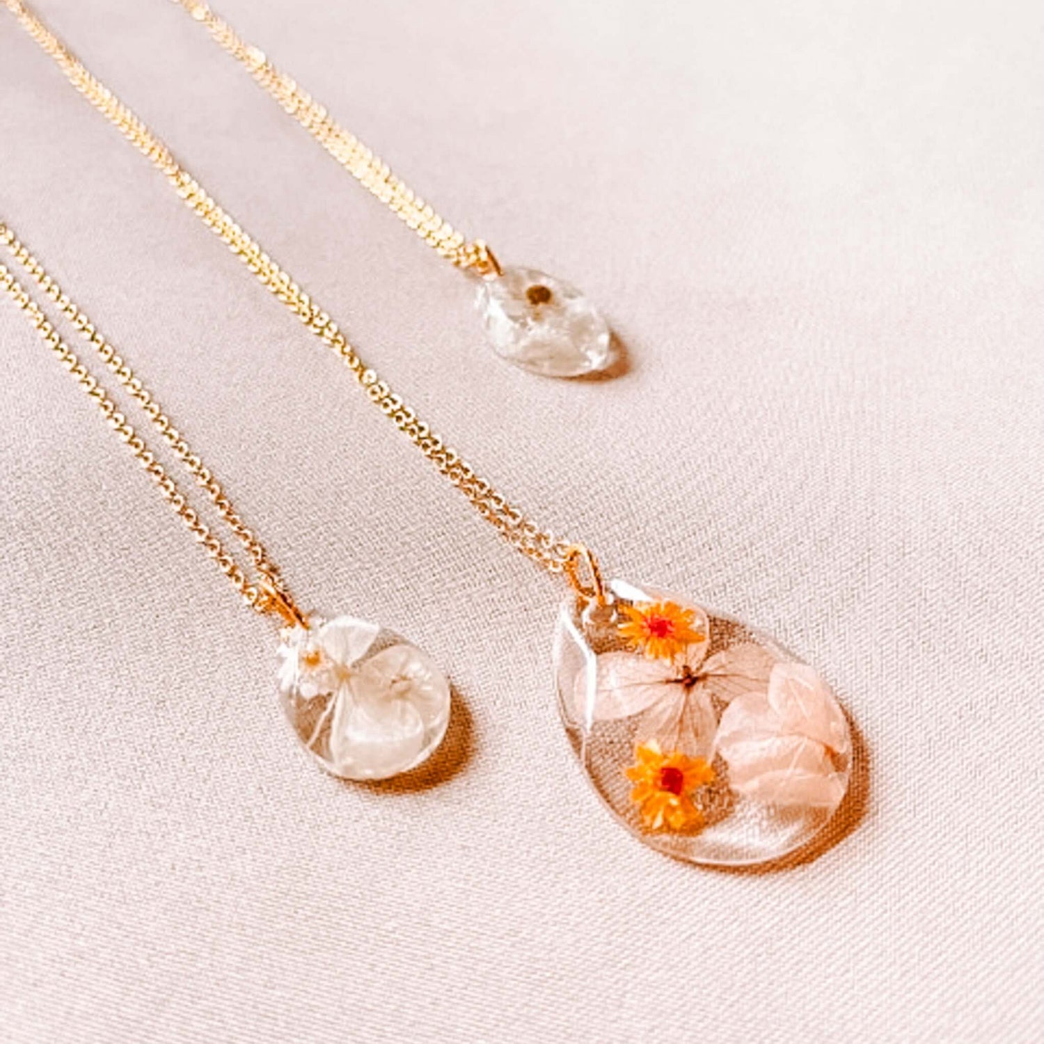 Drei Kettenanhänger mit Trockenblumen auf Tisch – uv harz schmuck, resin jewelry, auch für Firmenevents.