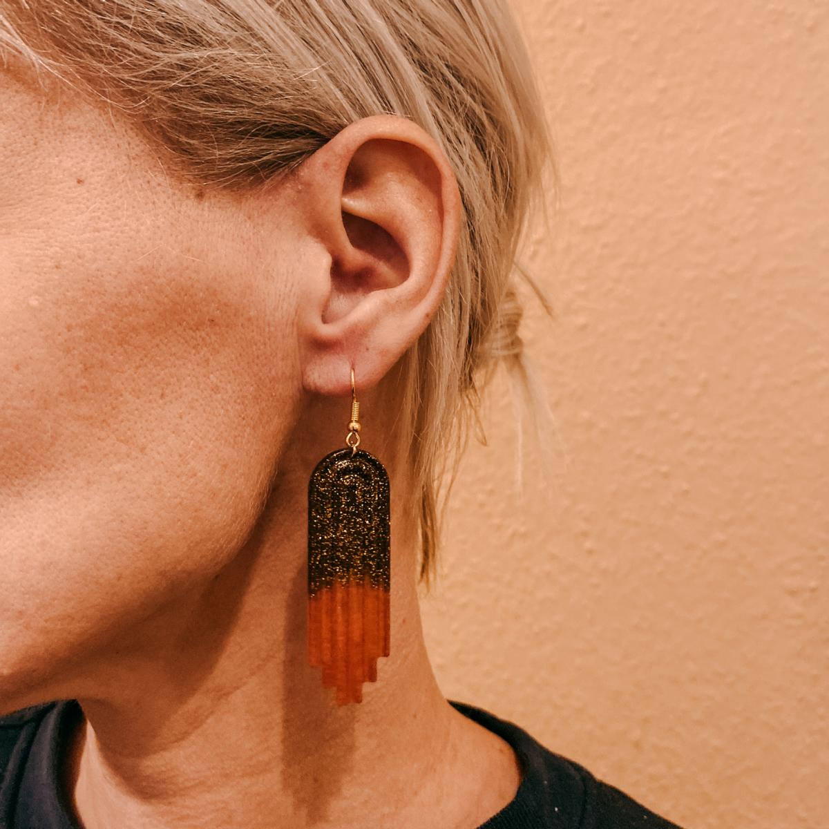 Nahaufnahme Ohr mit braun-rotem Glitzer Ohrring – handgemachter Resin Schmuck aus Workshop.