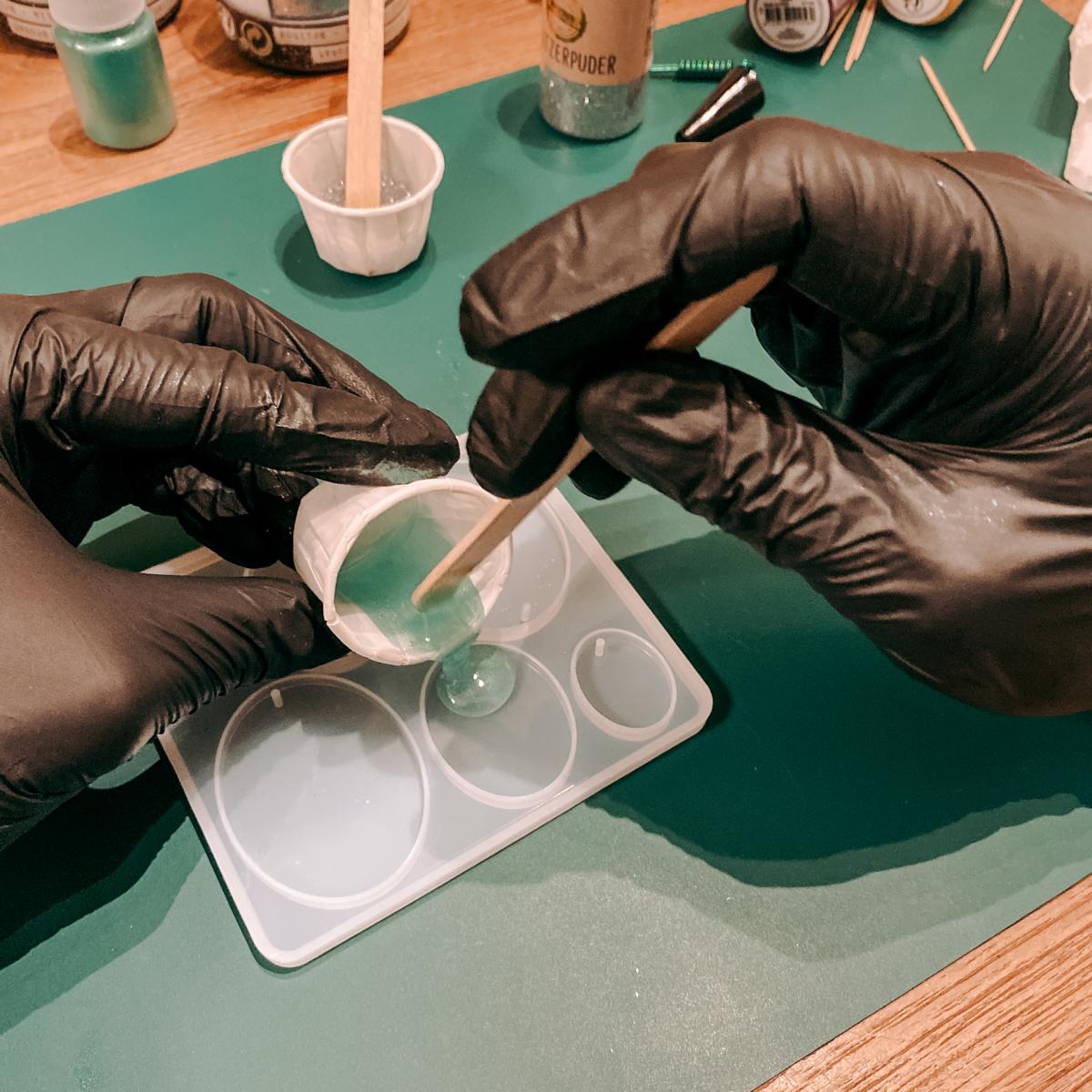 Zwei Hände füllen blaue Resin Mischung in Form – Epoxidharz Schmuck Workshop mit Farben und Glitzer.