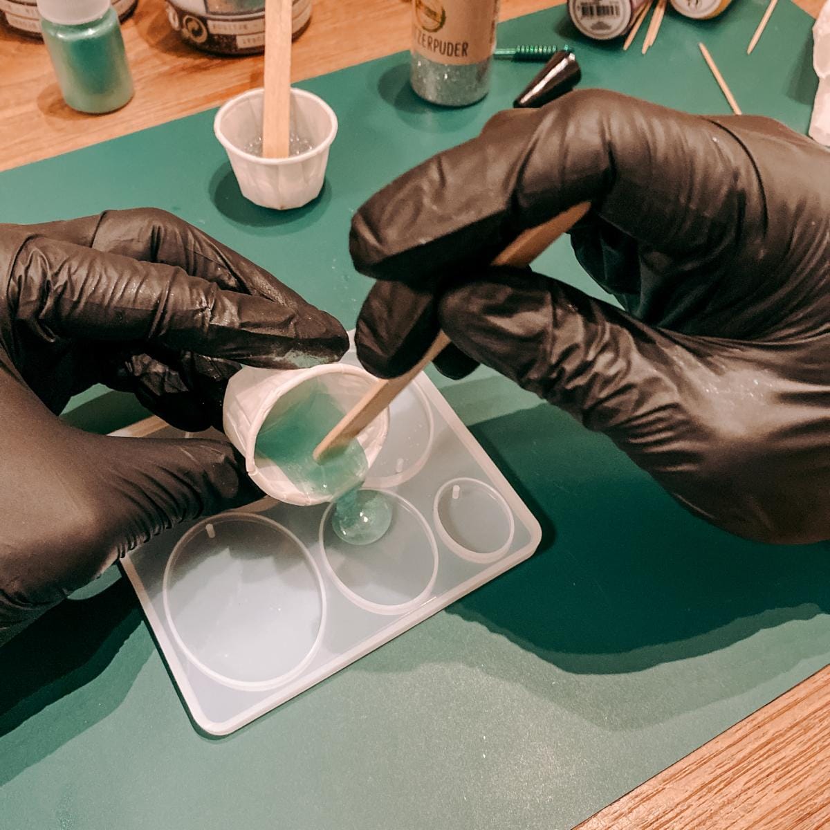 Zwei Hände füllen blaue Resin Mischung in Form – Epoxidharz Schmuck Workshop mit Farben und Glitzer.