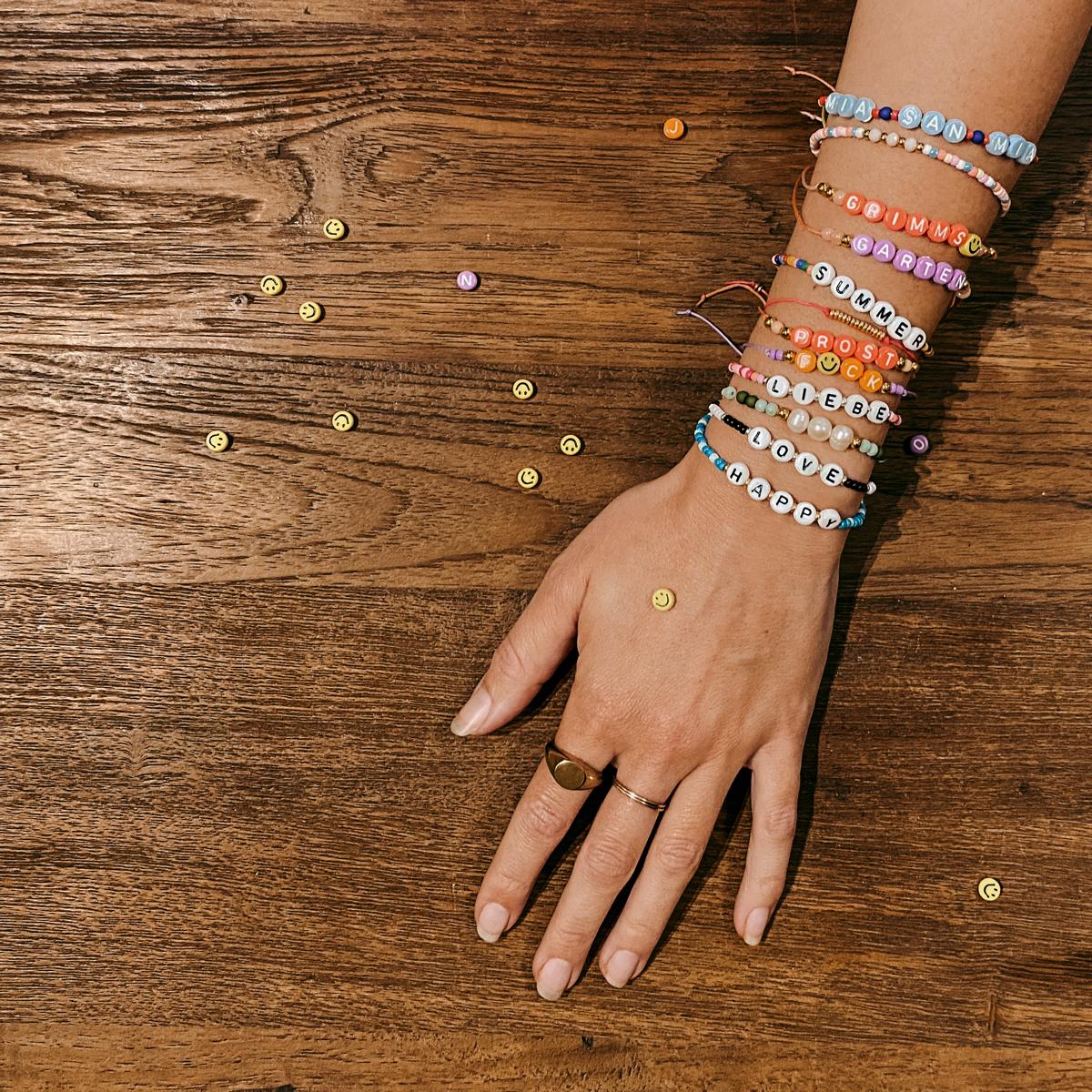 Hand mit vielen bunten Armbändern, Perlen auf Tisch – DIY Perlenschmuck Workshop Berlin, Armband kreativ.