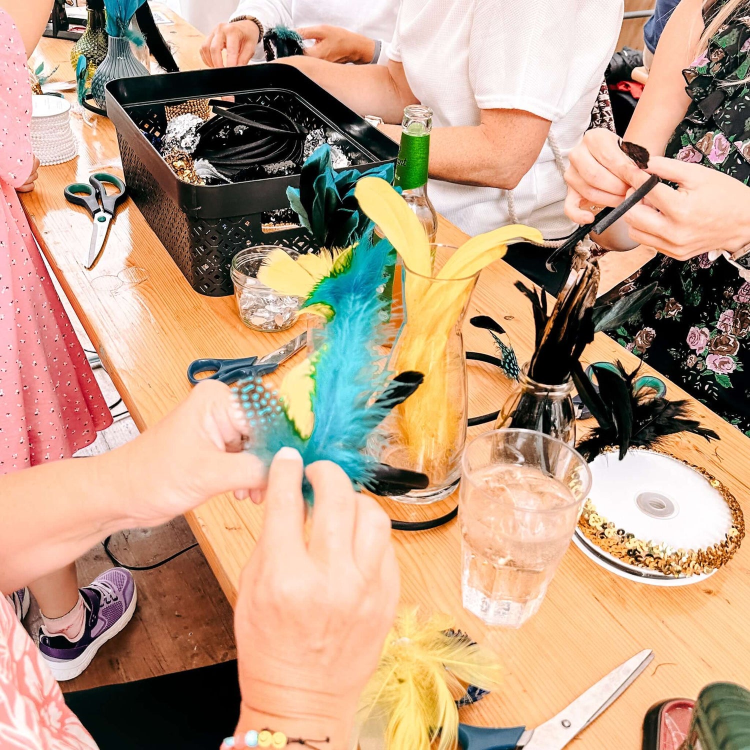 Mehrere Personen basteln Haarschmuck mit bunten Federn – kreatives 20er Jahre Teamevent oder JGA.